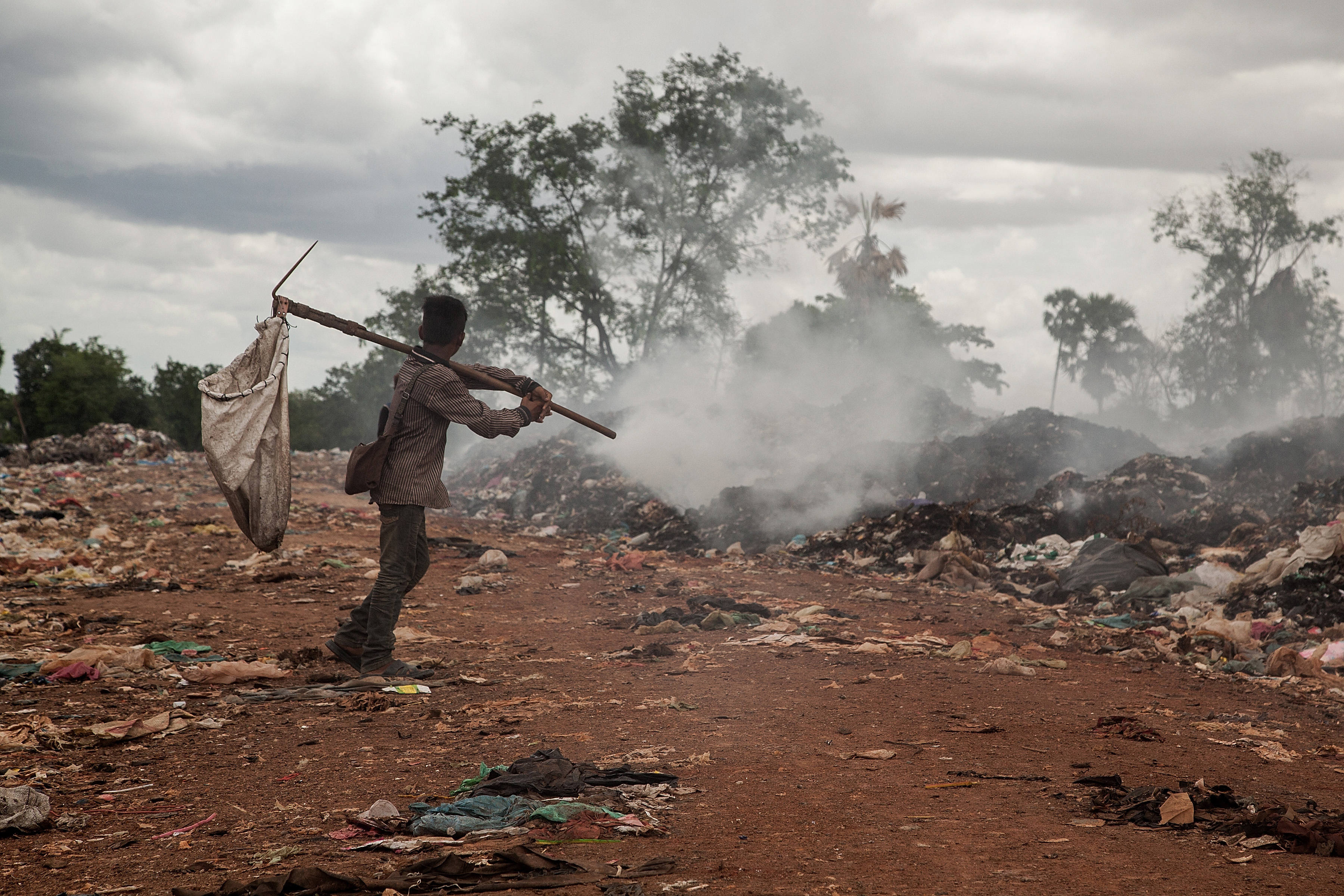 A young scavenger walks near a burning pile of trash in the Anlong Pi landfill on June 11, 2014 in Siem Reap, Cambodia. 