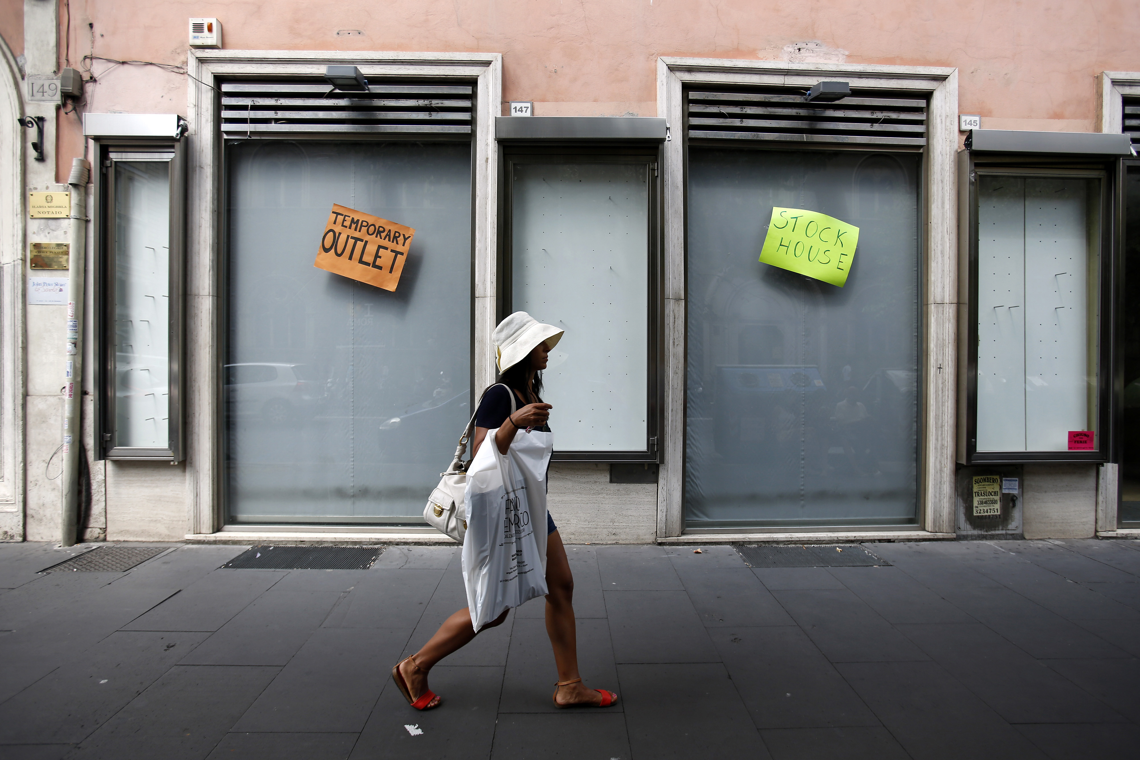 A pedestrian carries a plastic shopping bag as she passes a closed-down temporary outlet store in Rome, Italy, on Tuesday, Aug. 12, 2014. Italy's economy shrank 0.2 percent in the second quarter after contracting 0.1 percent in the previous three months. (Bloomberg—Bloomberg via Getty Images)