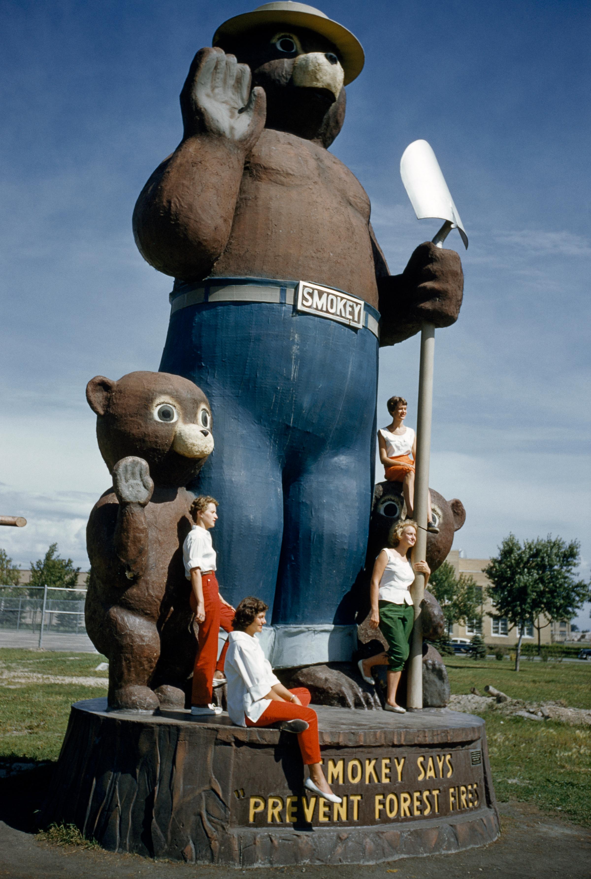 Young women pose on a giant statue of Smokey the Bear and his cubs
