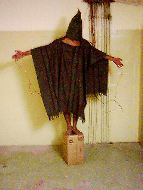 A photograph taken by U.S. Army Spc. Sabrina Harman shows an unidentified detainee standing on a box with a bag on his head and wires attached to him at the Abu Ghraib prison in Baghdad, Iraq. Sometime in 2003.