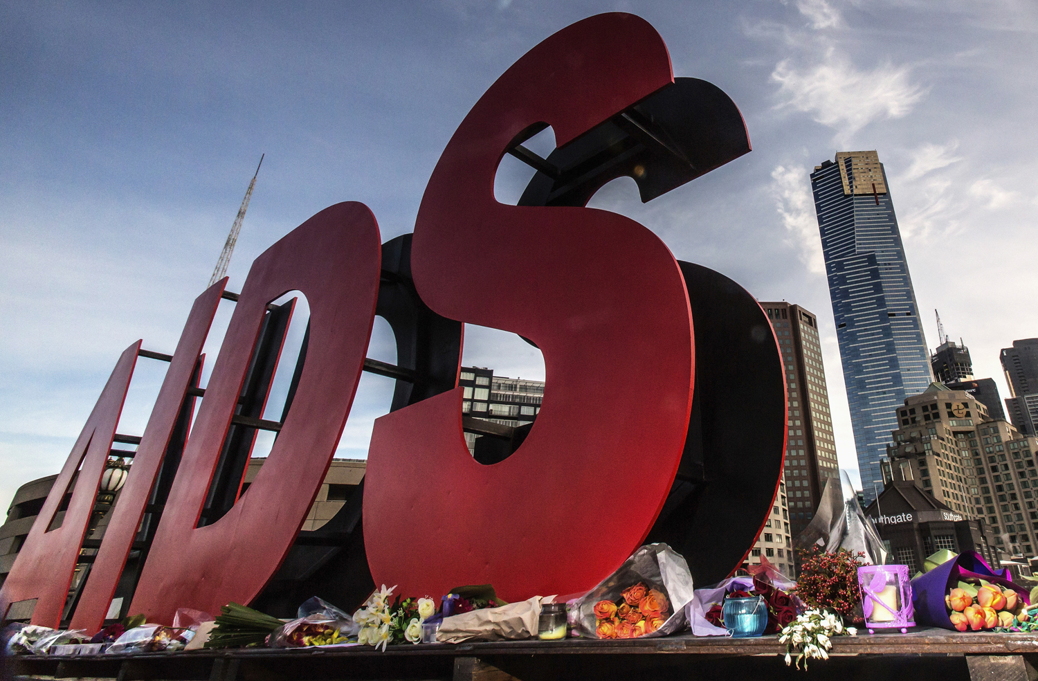 Flowers are laid as tributes to those killed in the Malaysia Airlines flight MH17, at the base of large sign for 20th International AIDS Conference in Melbourne