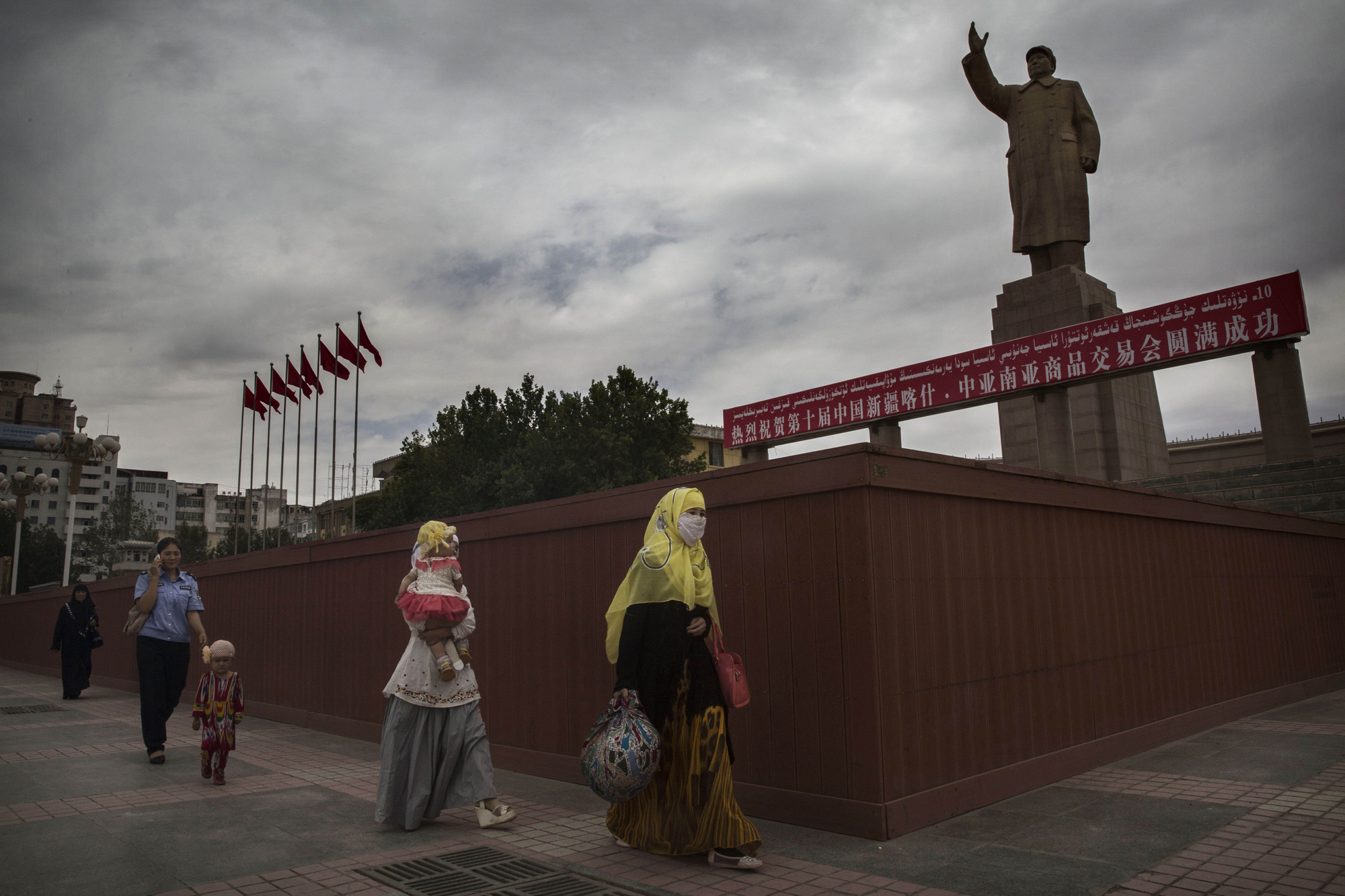 A veiled Muslim Uyghur woman walks passed a statue of Mao Zedong on July 31, 2014 in Kashgar.