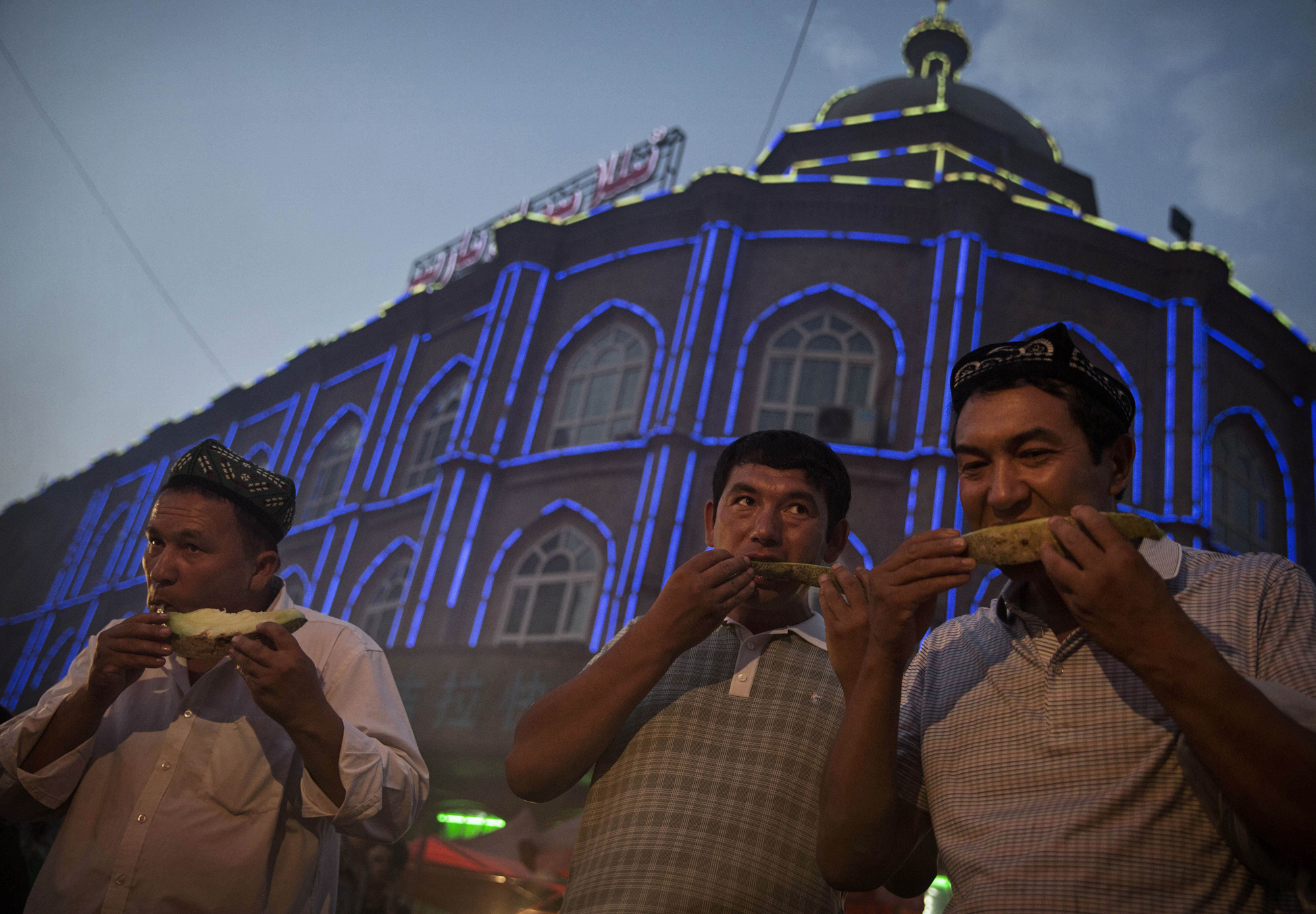 Uyghur men eat melon as they break their Ramadan fast before the Eid holiday at a night market on July 28, 2014 in old Kashgar.
