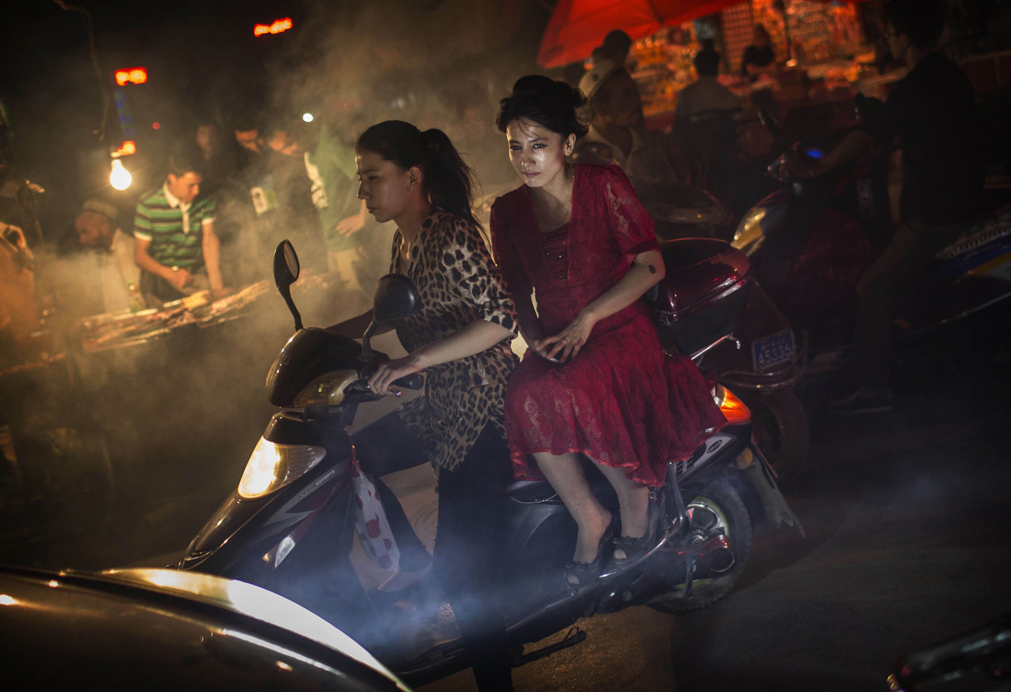 Uyghur women without veils ride on a scooter in a market on July 27, 2014 in old Kashgar.