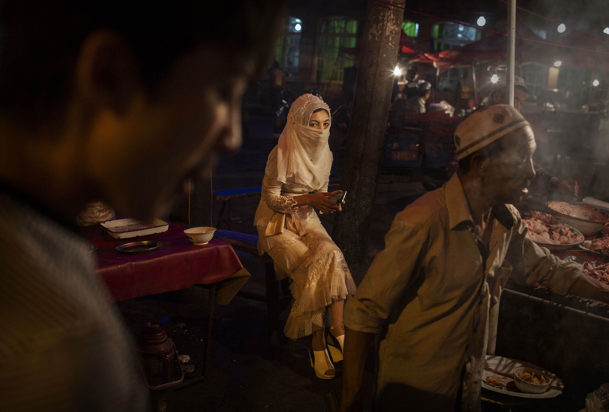 A veiled Uighurwoman sits at a food stall at a local market on August 1, 2014 in Kashgar.