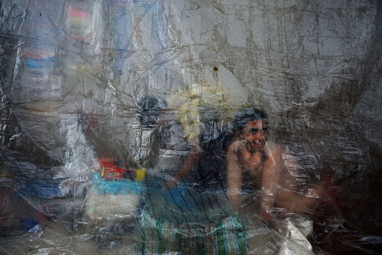 Aug. 28, 2014. Indian youths assisting at a shop shelter from rain behind a plastic tarpaulin in New Delhi.