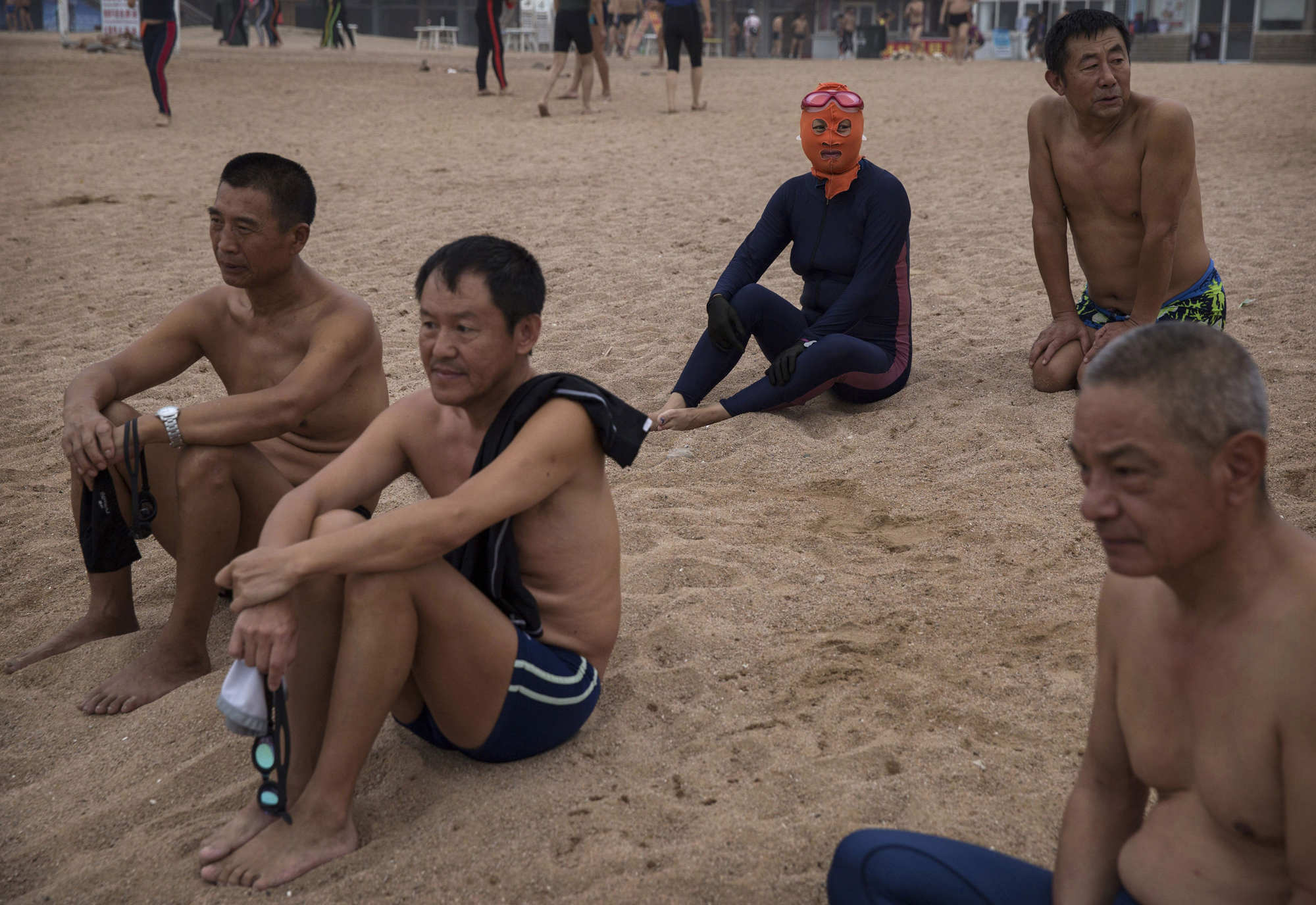 A woman wearing a facekini sits next to men on the beach on Aug. 20, 2014, on the Yellow Sea in Qingdao.