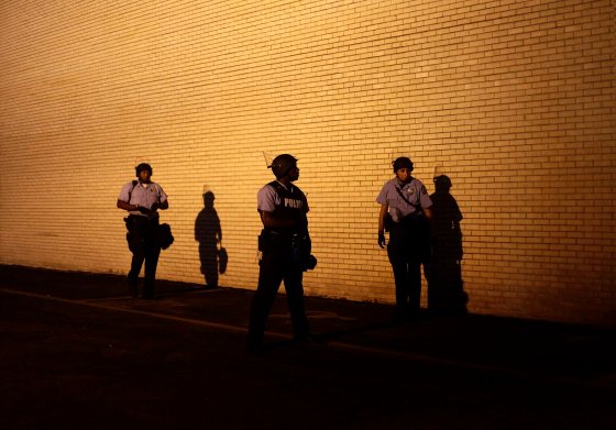 Police officers in riot gear watch demonstrators protesting against the shooting of Michael Brown from the side of a building in Ferguson
