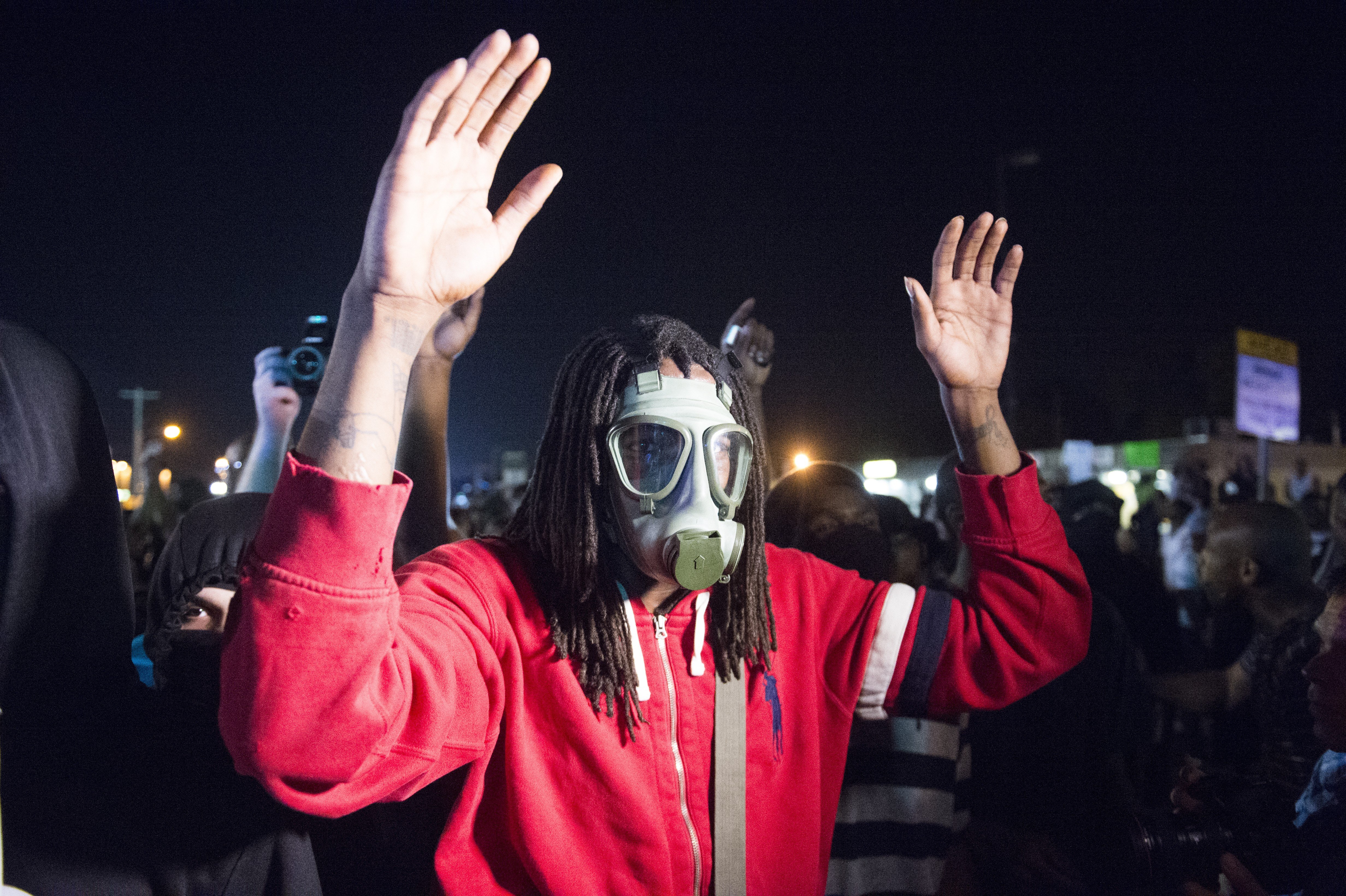 A protestor wearing a gas mask stands with his hands up while facing armed police in Ferguson, Mo. on Aug. 18, 2014.