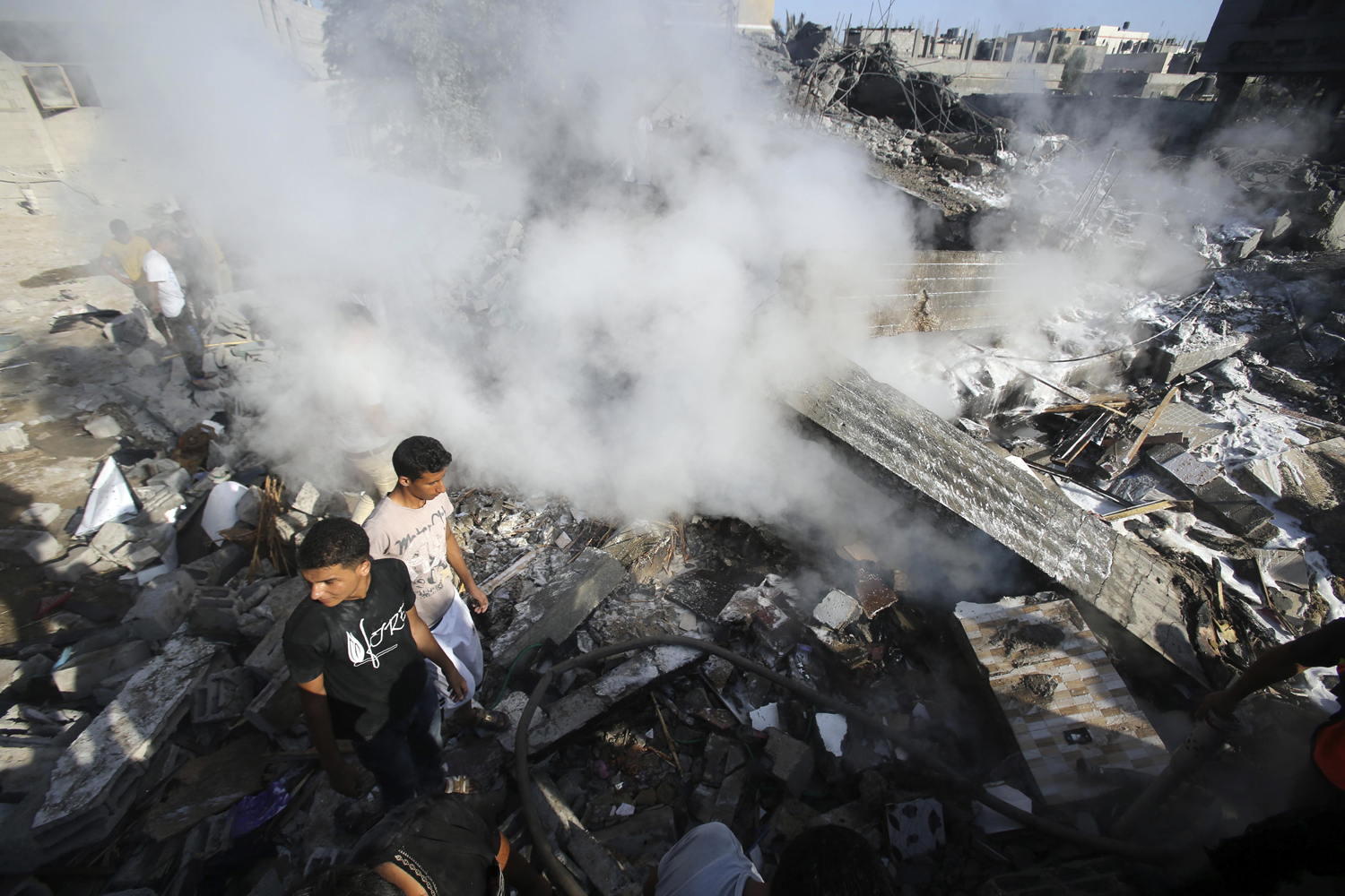 Smoke rises as Palestinians stand atop the rubble of a house, which witnesses said was destroyed in an Israeli air strike, in Rafah in the southern Gaza Strip