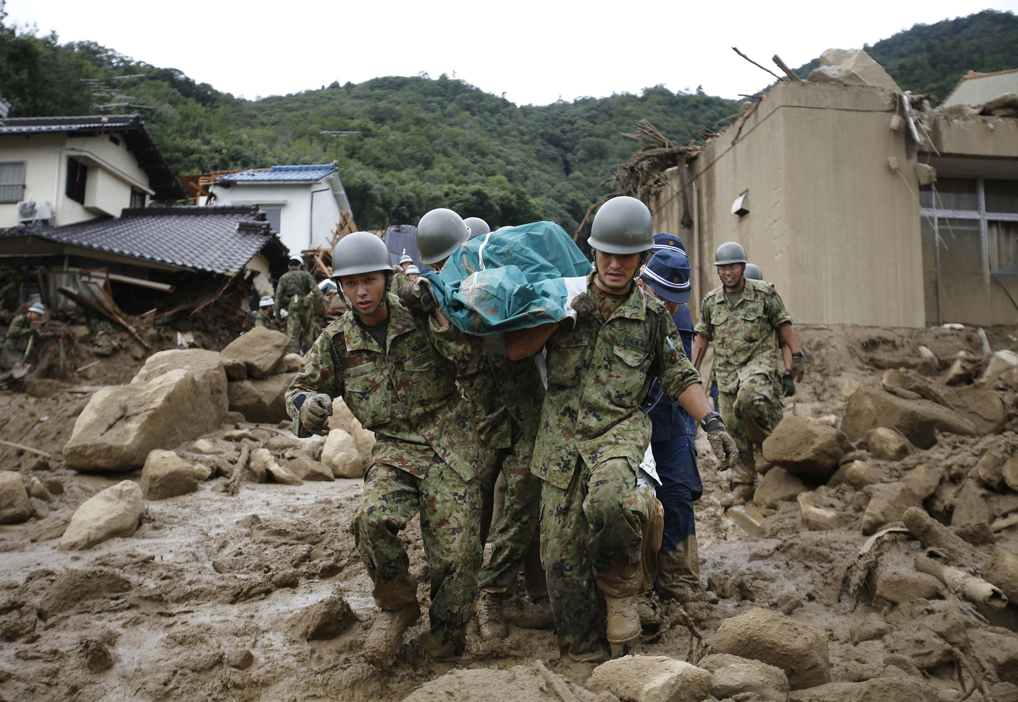Japan Self-Defense Force soldiers and police officers carry the body of a victim in a plastic bag at a site where a landslide swept through a residential area at Asaminami ward in Hiroshima, western Japan, Aug. 20, 2014.