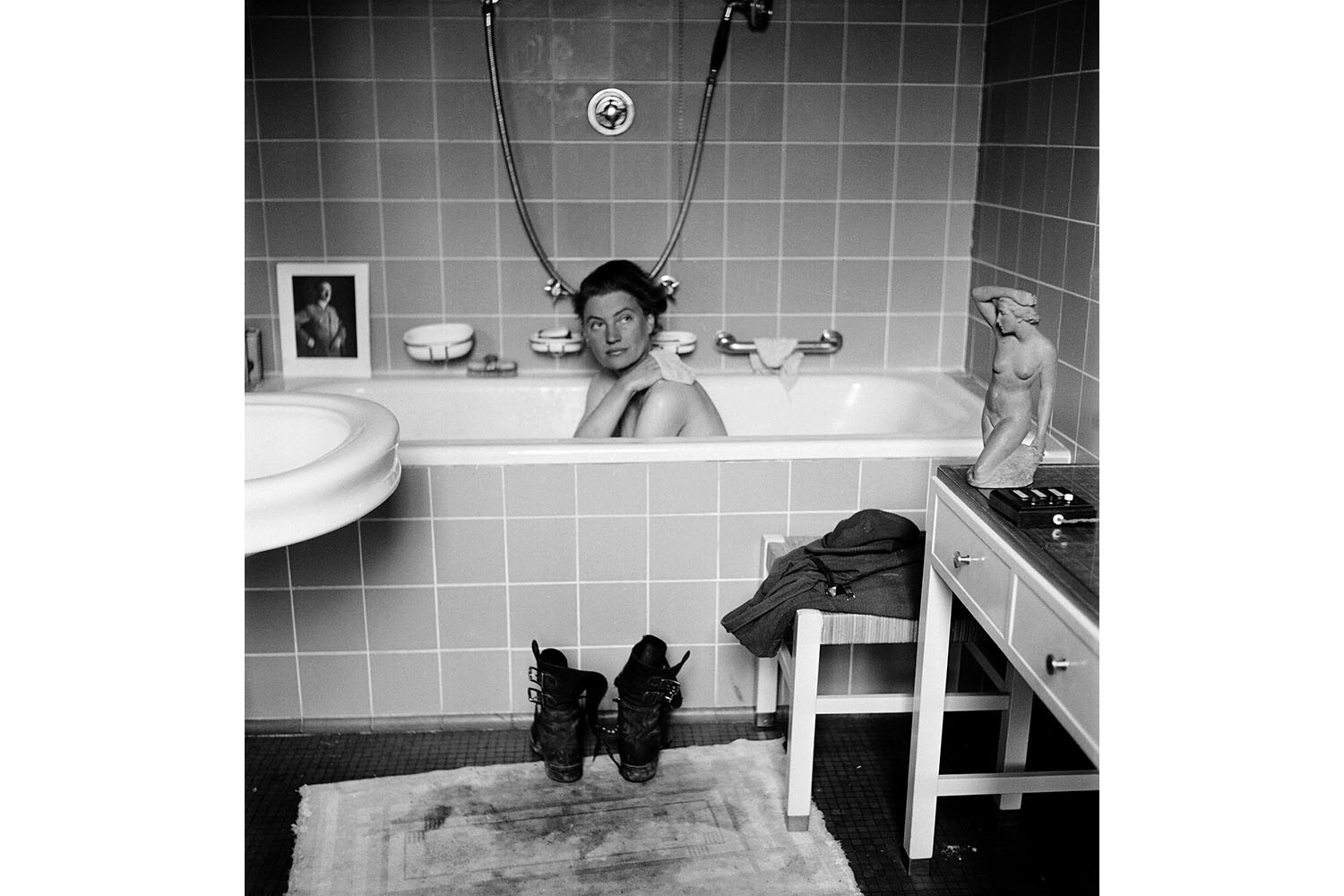 From Lee Miller's War published by Thames &amp; Hudson. Lee Miller in Hitler’s apartment at 16 Prinzregentenplatz. Note the combat boots on the bath mat now stained with the dust of Dachau; and a photograph of the previous owner of the flat propped on the edge of the tub.