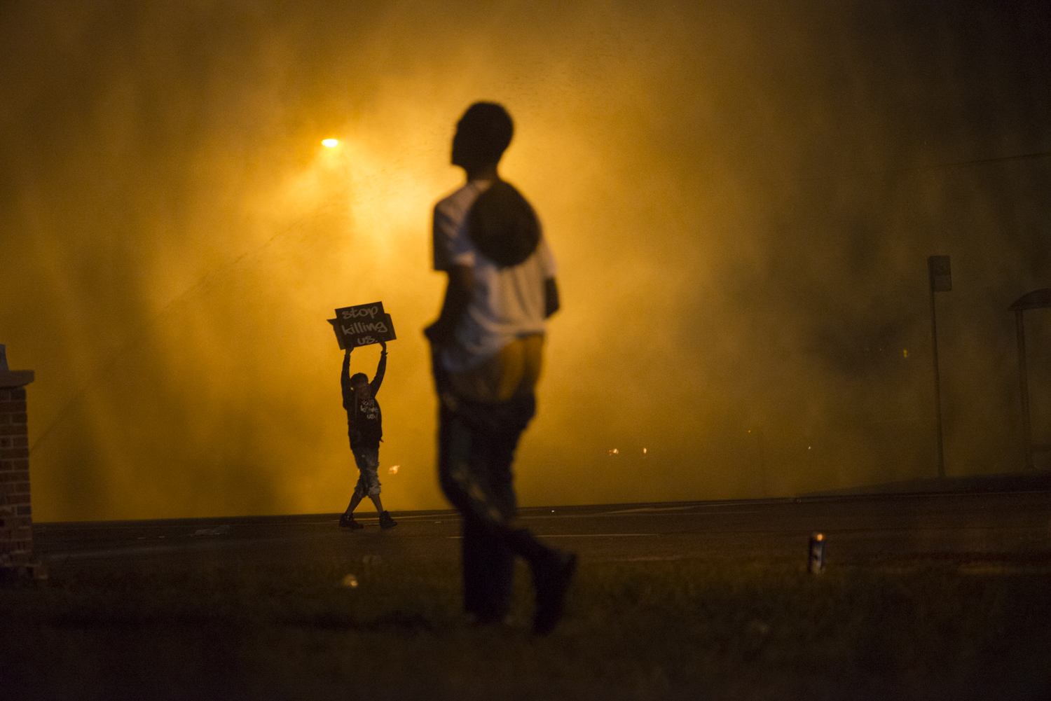 A protestor holds a sign that reads "stop killing us" amid clouds of tear gas in Ferguson, Mo. on Aug. 17, 2014. (Jon Lowenstein—Noor for TIME)