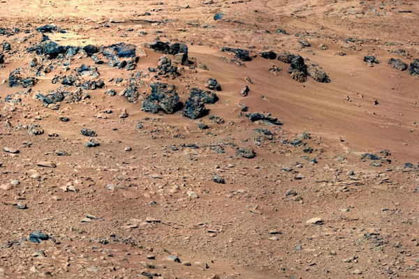 This patch of windblown sand and dust downhill from a cluster of dark rocks is the "Rocknest" site, which was the location for the first use of the scoop on the arm of Curiosity.