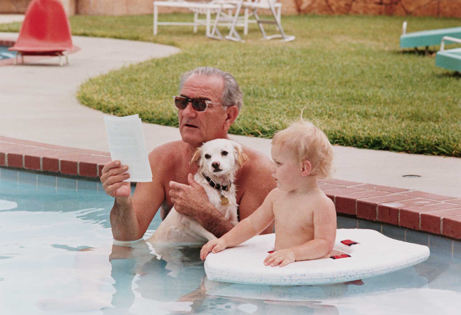 President Lyndon B. Johnson relaxes in his pool with his grandson Lyn and the First Family's new dog, Yuki.
