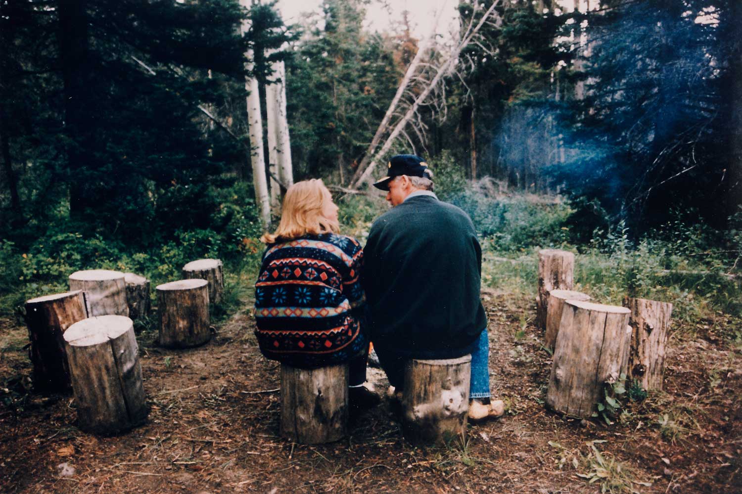 Rear view of Pres. Bill Clinton and First Lady Hillary Rodham Clinton wearing casual clothes and sitting on tree stumps while on vacation.