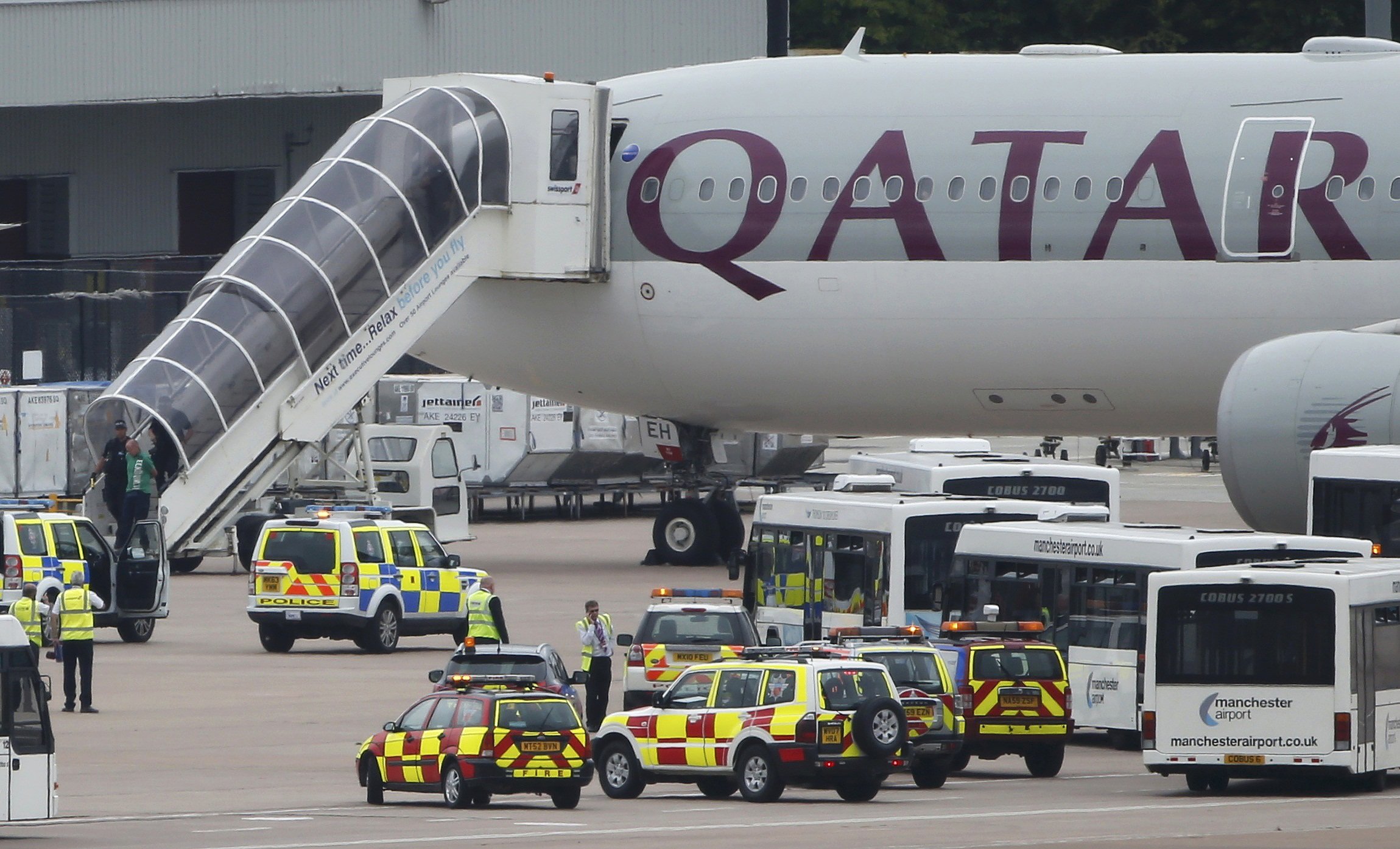 A man is escorted off a Qatar Airways aircraft by police at Manchester airport in Manchester, England on August 5, 2014. A British fighter jet escorted a passenger plane into Manchester airport on Tuesday after the pilot reported that a suspect device was possibly on board.