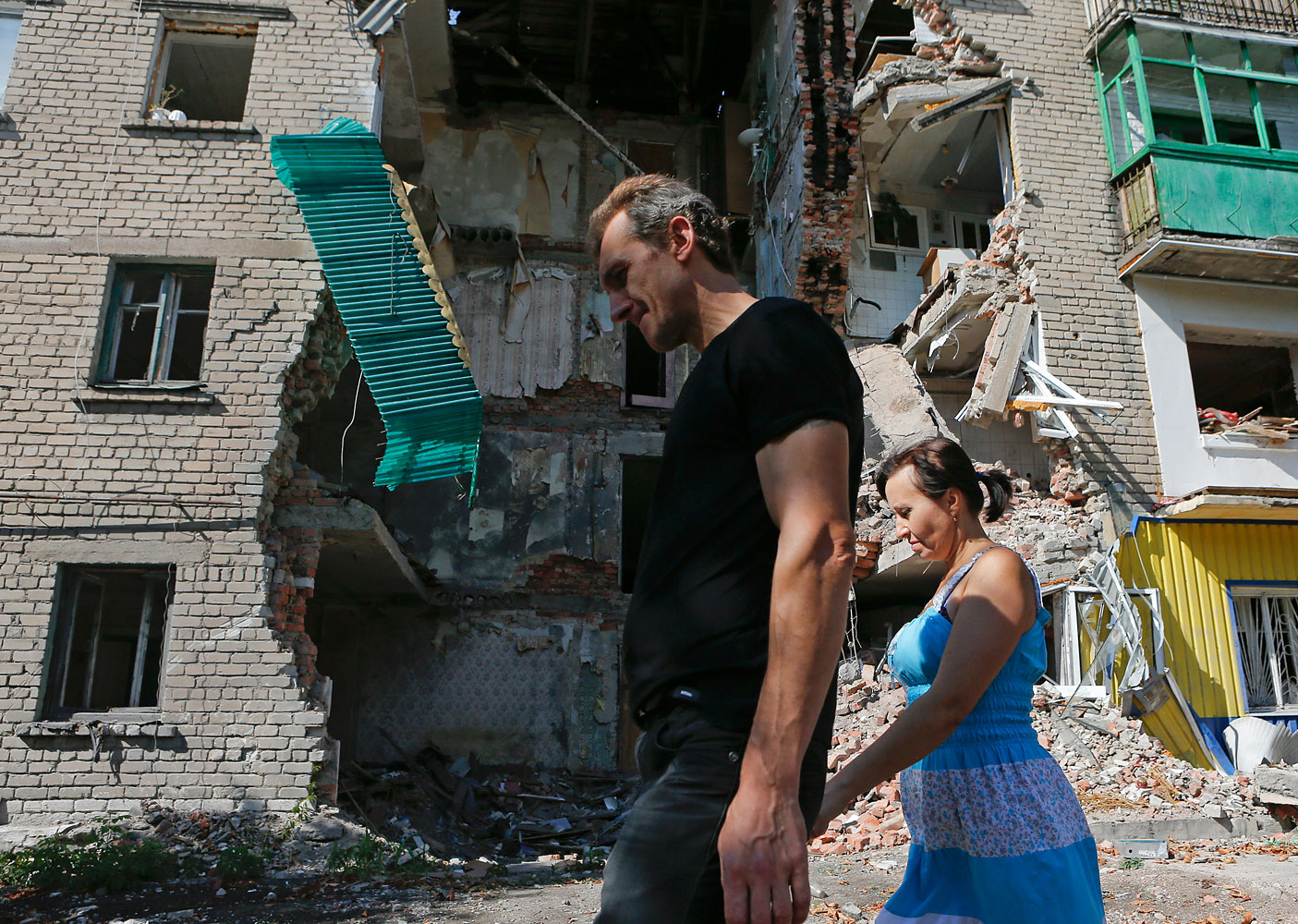 People walk past a building damaged by shelling in Snizhne (Snezhnoye), Donetsk region