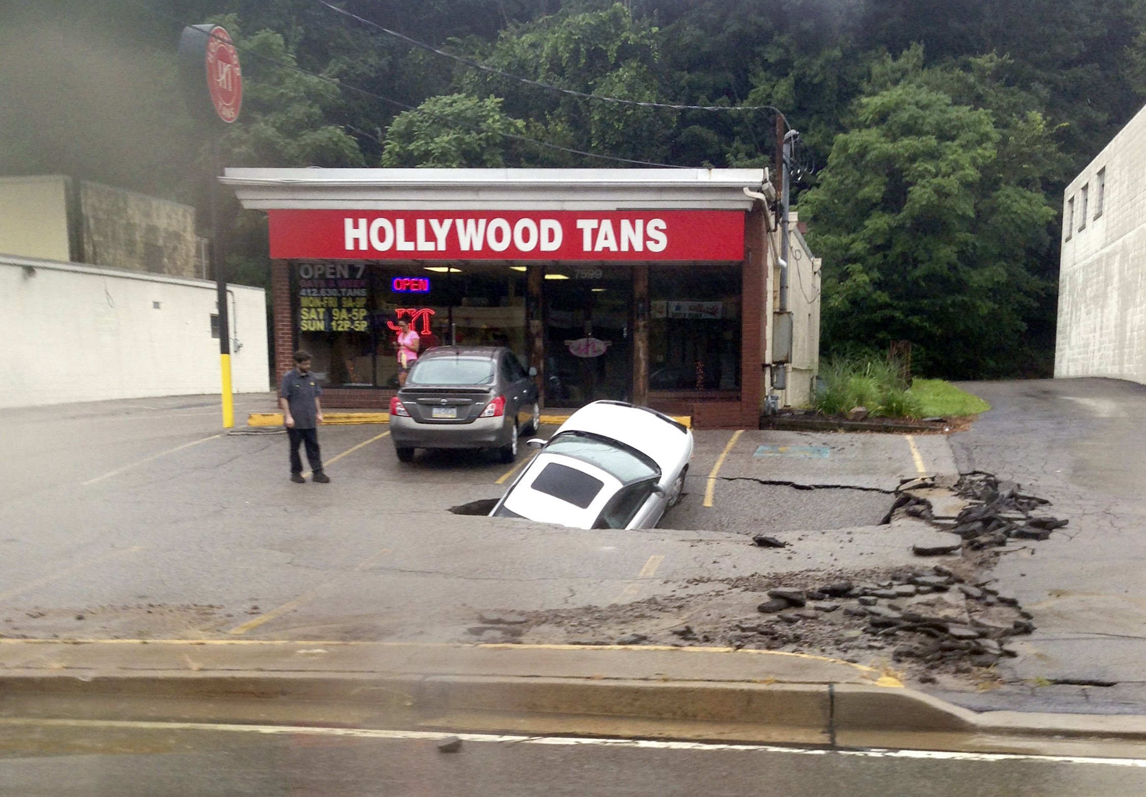 A man looks at a car as it falls into a sinkhole on McKnight Road in Ross Township of Pittsburgh on Aug. 12, 2014.