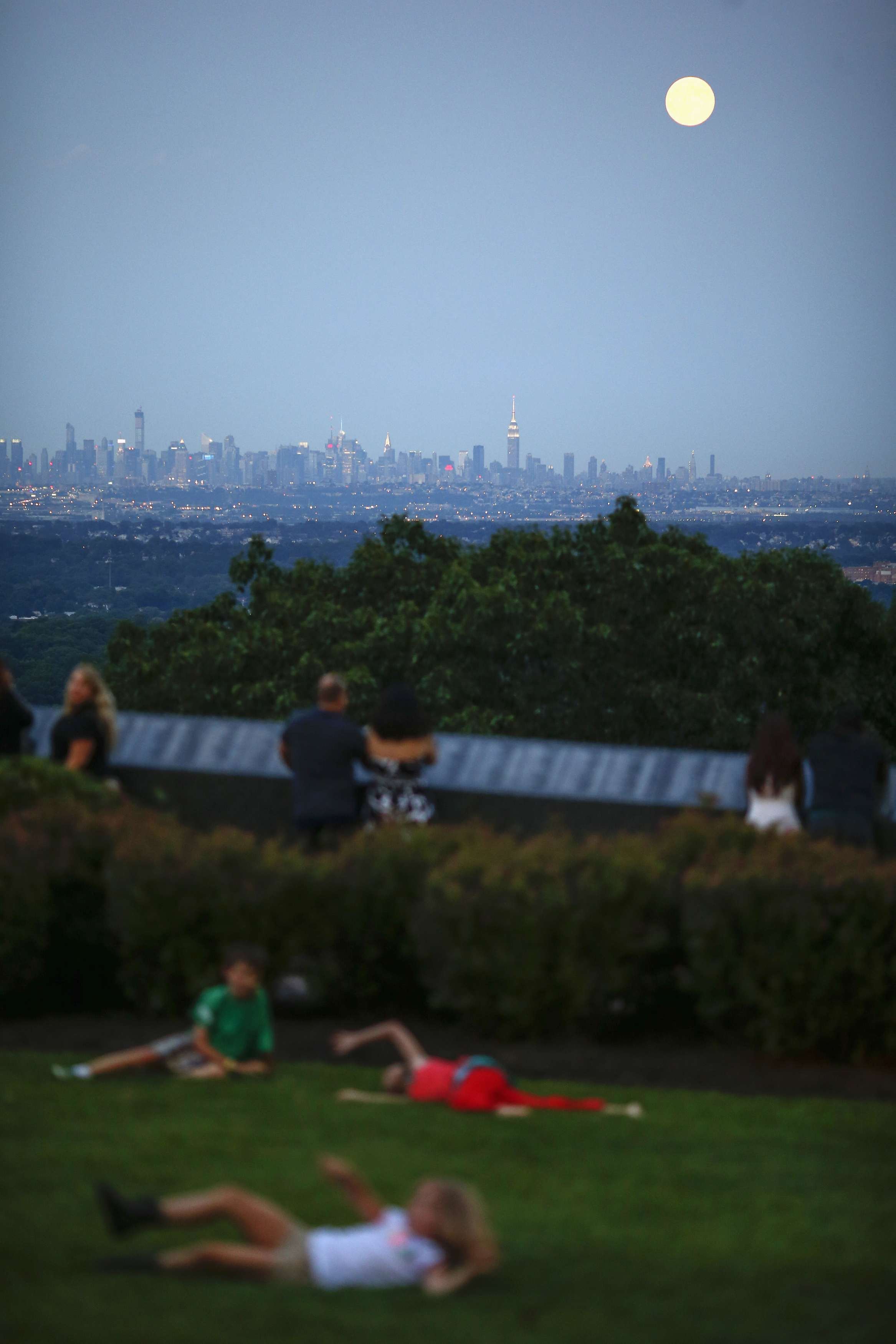 Children play on the grass while a full moon known as "supermoon" rises over the skyline of New York and the Empire State Building, as seen from the Eagle Rock Reservation in West Orange, New Jersey on August 10, 2014.