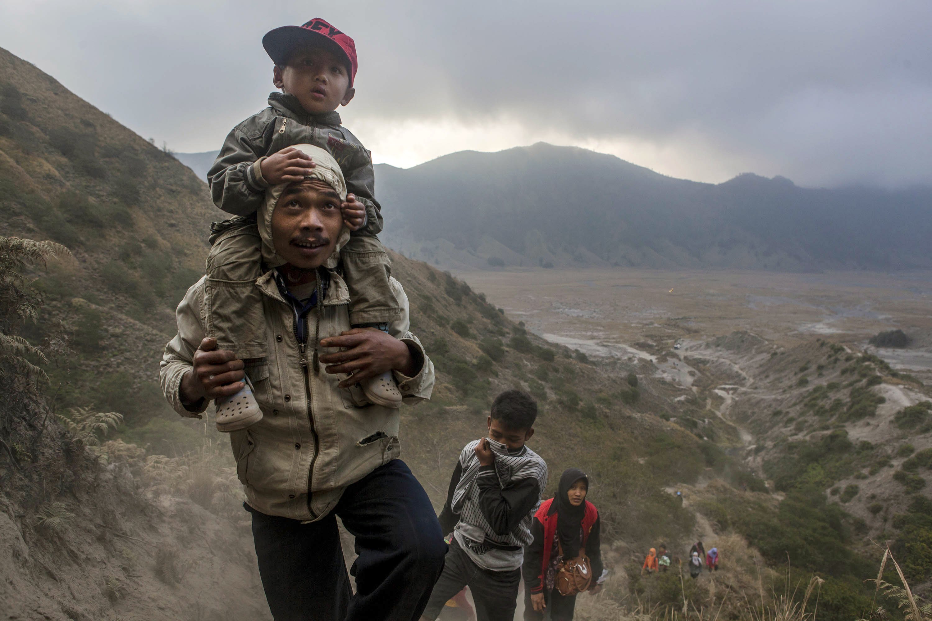A Tenggerese worshipper carries his son as he walk climb the mountain for collect holy water during the Tenggerese Hindu Yadnya Kasada festival on August 11, 2014 in Probolinggo, Java, Indonesia.