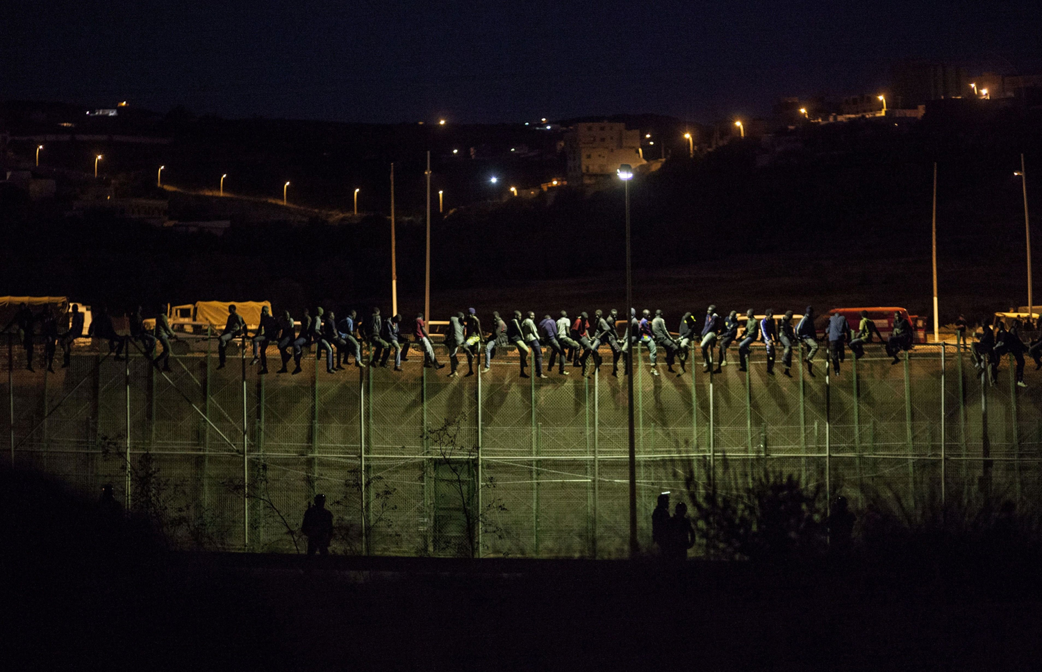Aug. 13, 2014.  
                              Spanish Guardia Civil watch as would be immigrants from Africa sit atop a wire-meche fence after scrambling over two other border barriers on Spain's tiny north African enclave of Melilla.