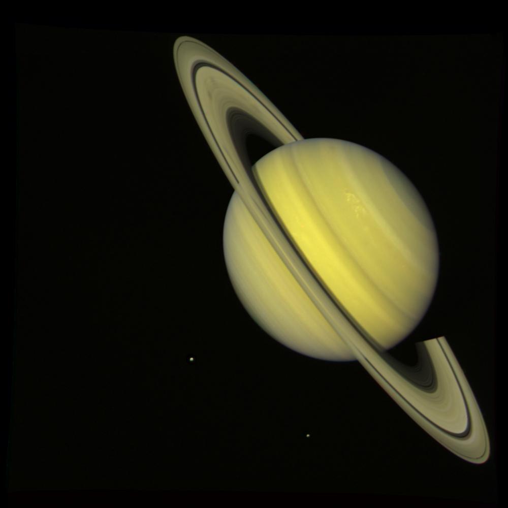 NASA's Voyager 2 took this 'true color' photograph of Saturn on July 21, 1981, when the spacecraft was 33.9 million kilometers (21 million miles) from the planet. Two bright, presumably convective cloud patterns are visible in the mid-northern hemisphere and several dark spoke-like features can be seen in the broad B-ring (left of planet). The moons Rhea and Dione appear as blue dots to the south and southeast of Saturn, respectively. Voyager 2 made its closest approach to Saturn on Aug. 25, 1981. The Voyager project is managed for NASA by the Jet Propulsion Laboratory, Pasadena, Calif.
