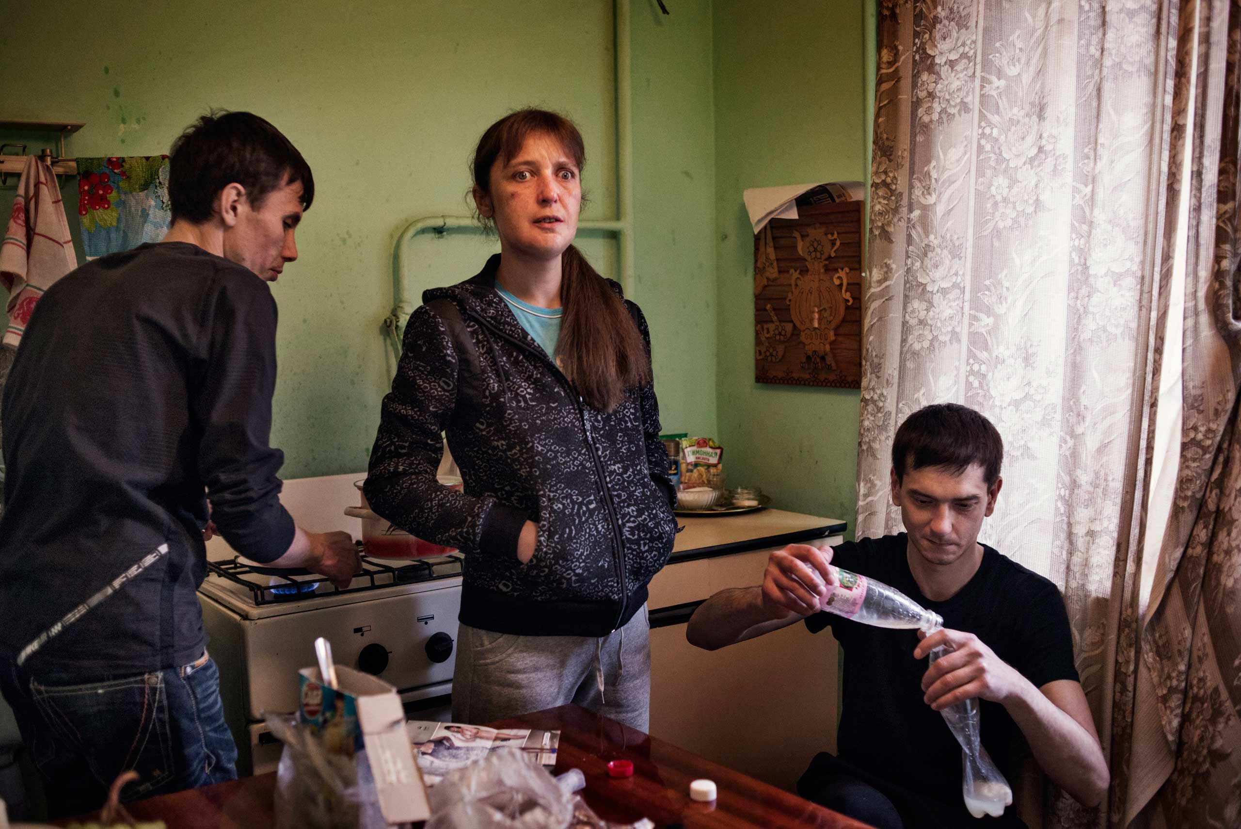 From the left, Alexey, Natalya, 34 years old, and her husband Ilya, 34 years old, prepare krokodil in a kitchen.