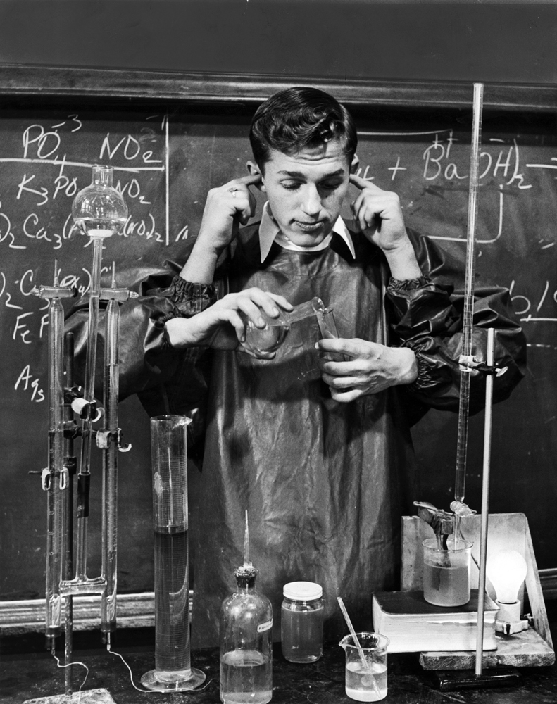 Amusing the class when teacher is out of room, Earl stops up ears with two of his hands as he mixes a fake chemical formulae with his two other hands.