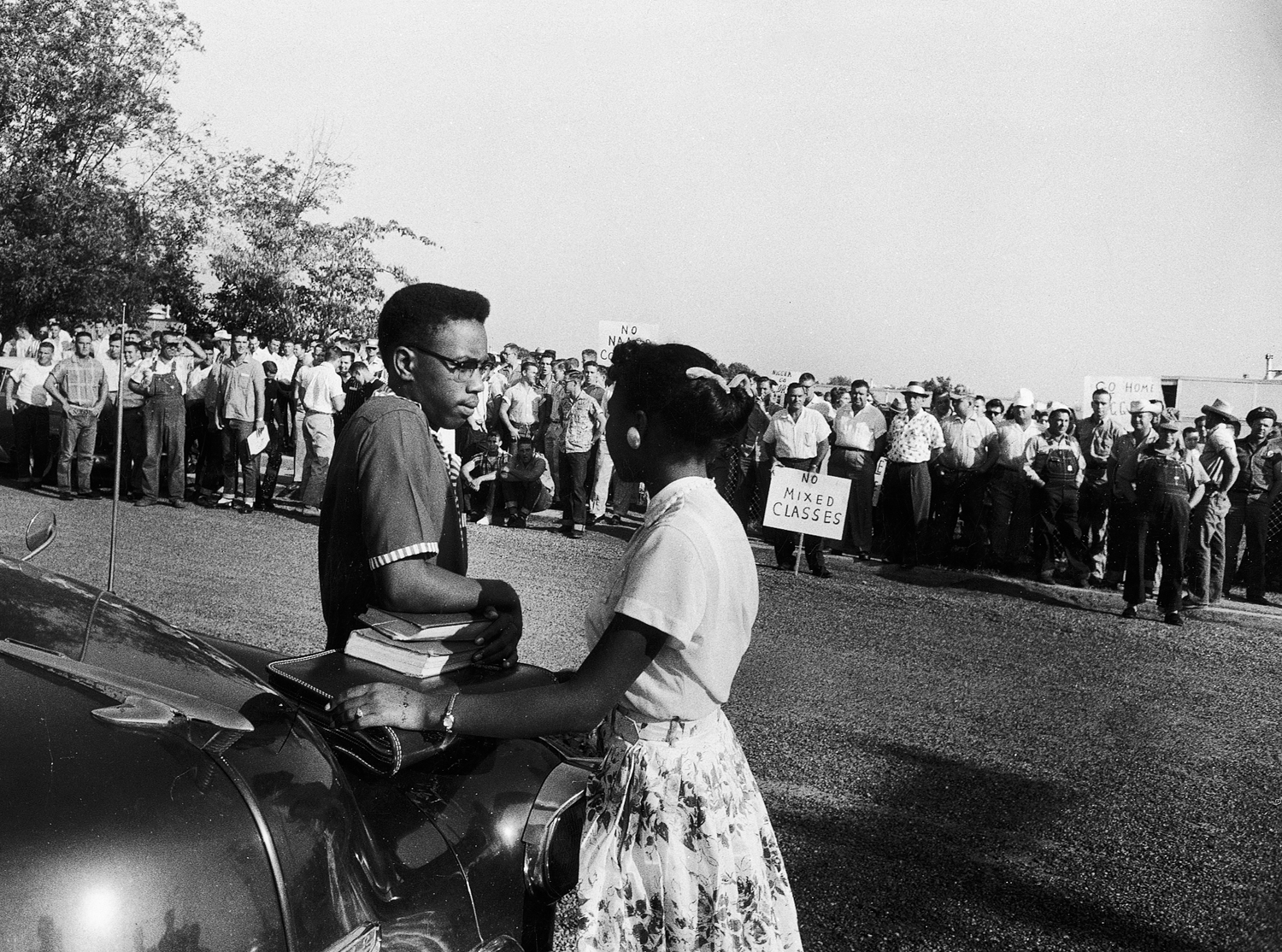 Students Steve Posten, 17, and Jessalyn Gray, 18, wait tensely beside a cab while a crowd of whites taunts them outside Texarkana Junior College, Texarkana, Tex., 1956. Jessalyn eventually asked police to escort them inside. When the police refused, the students left.