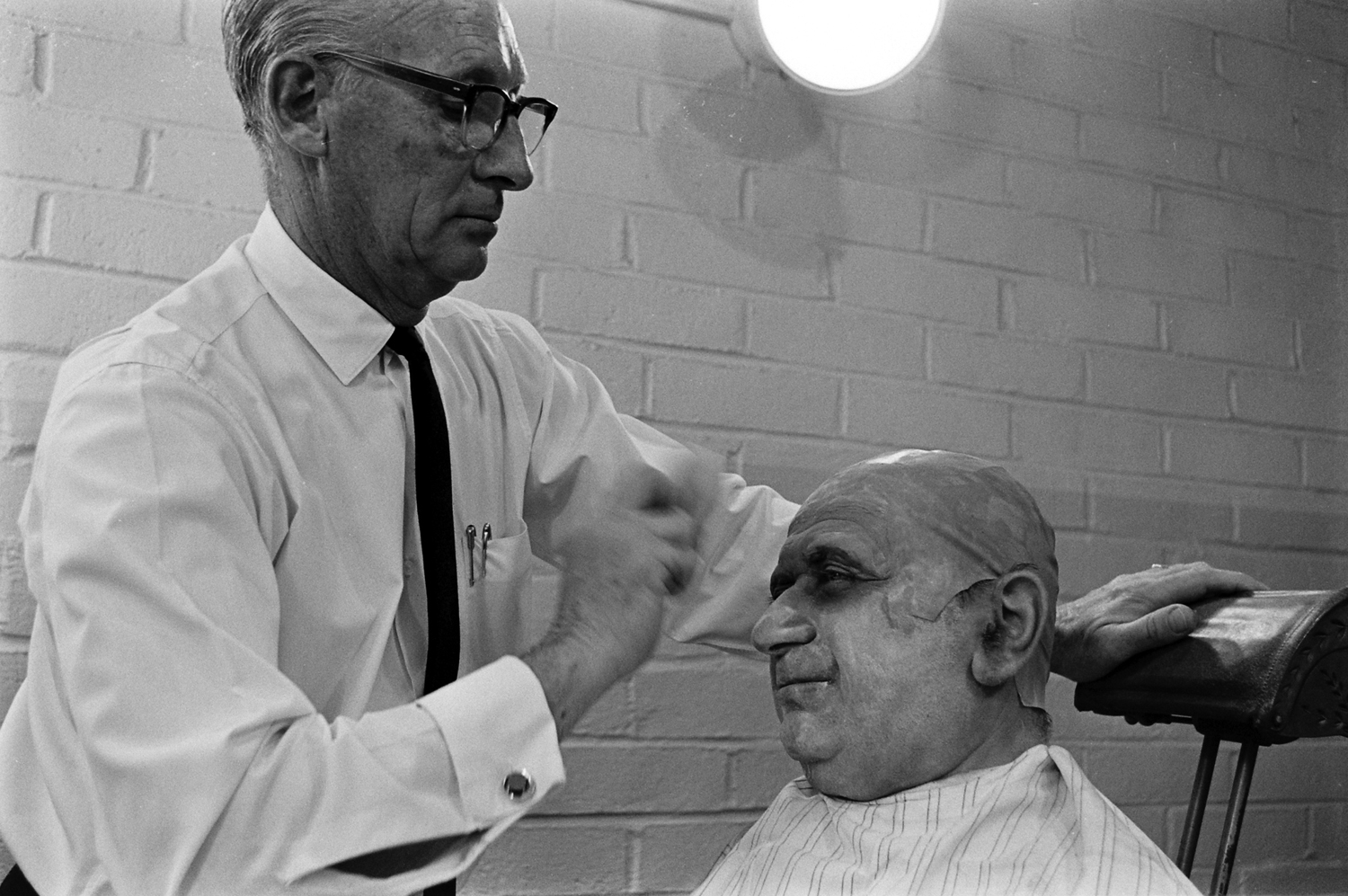 A makeup artist with actor (possibly Jackie Coogan) auditioning for the role of Uncle Fester, 1964.