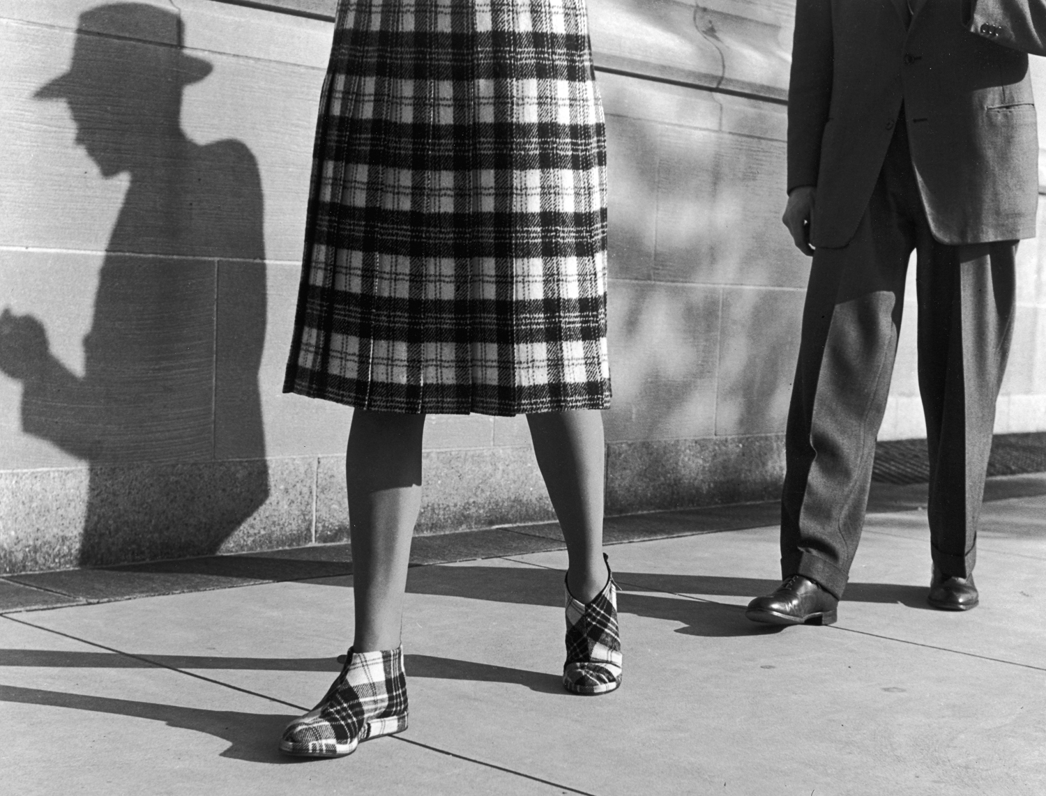 A woman in a plaid skirt and matching shoes, shadowed by a stranger, New York City, 1946.