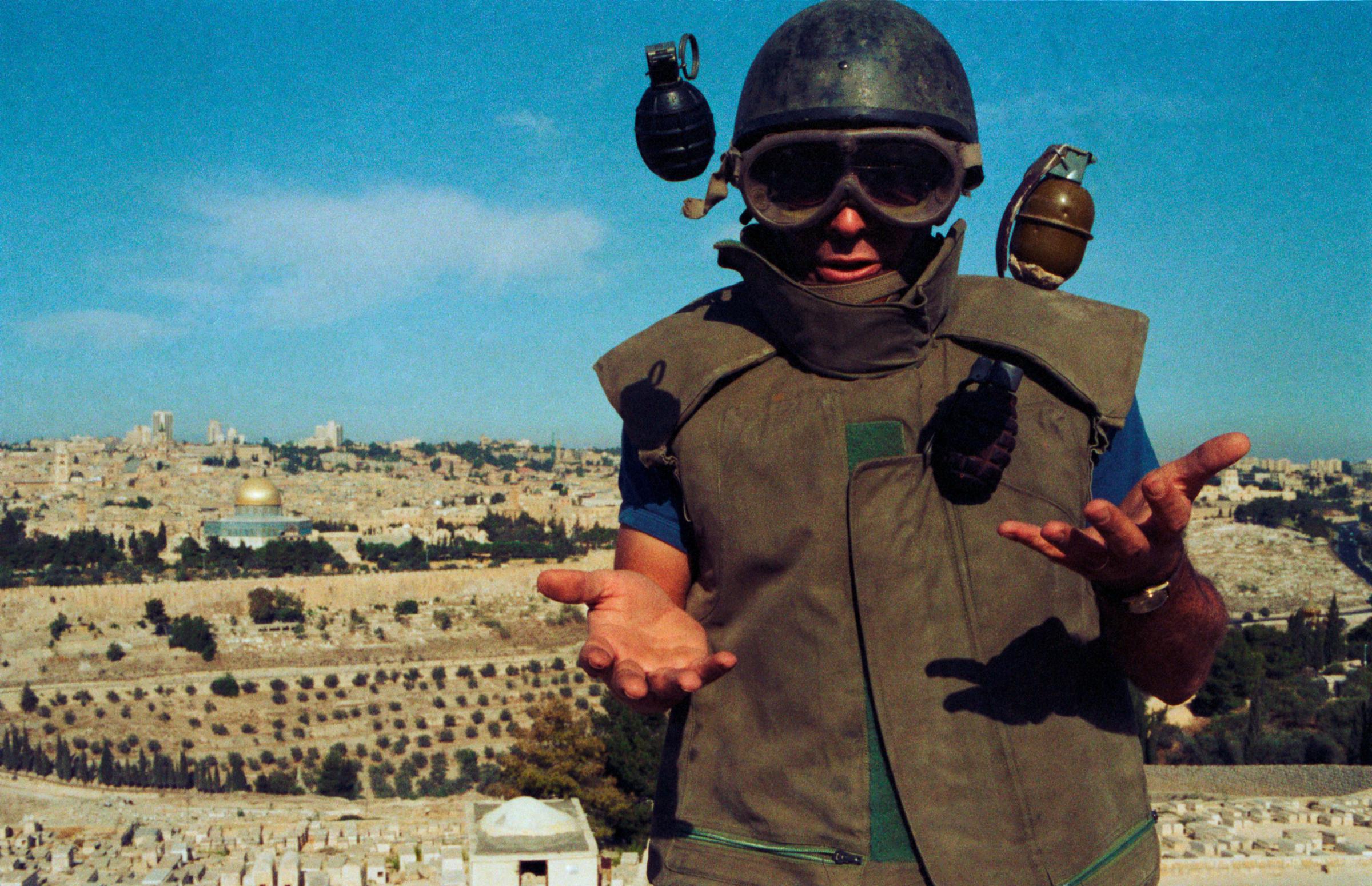 Dressed in bomb-squad protective gear, Uri tries to learn how to juggle using three hand grenades on a hill above the holy city. A year ago a terrorist-planted bomb exploded in a bus carrying Jews through West Jerusalem. “I arrived two minutes after the explosion,” says Uri. “There were shoes, fingers, glasses, blood. It was hell.” During the last 12 months the team has defused 36 other such devices. [1984]