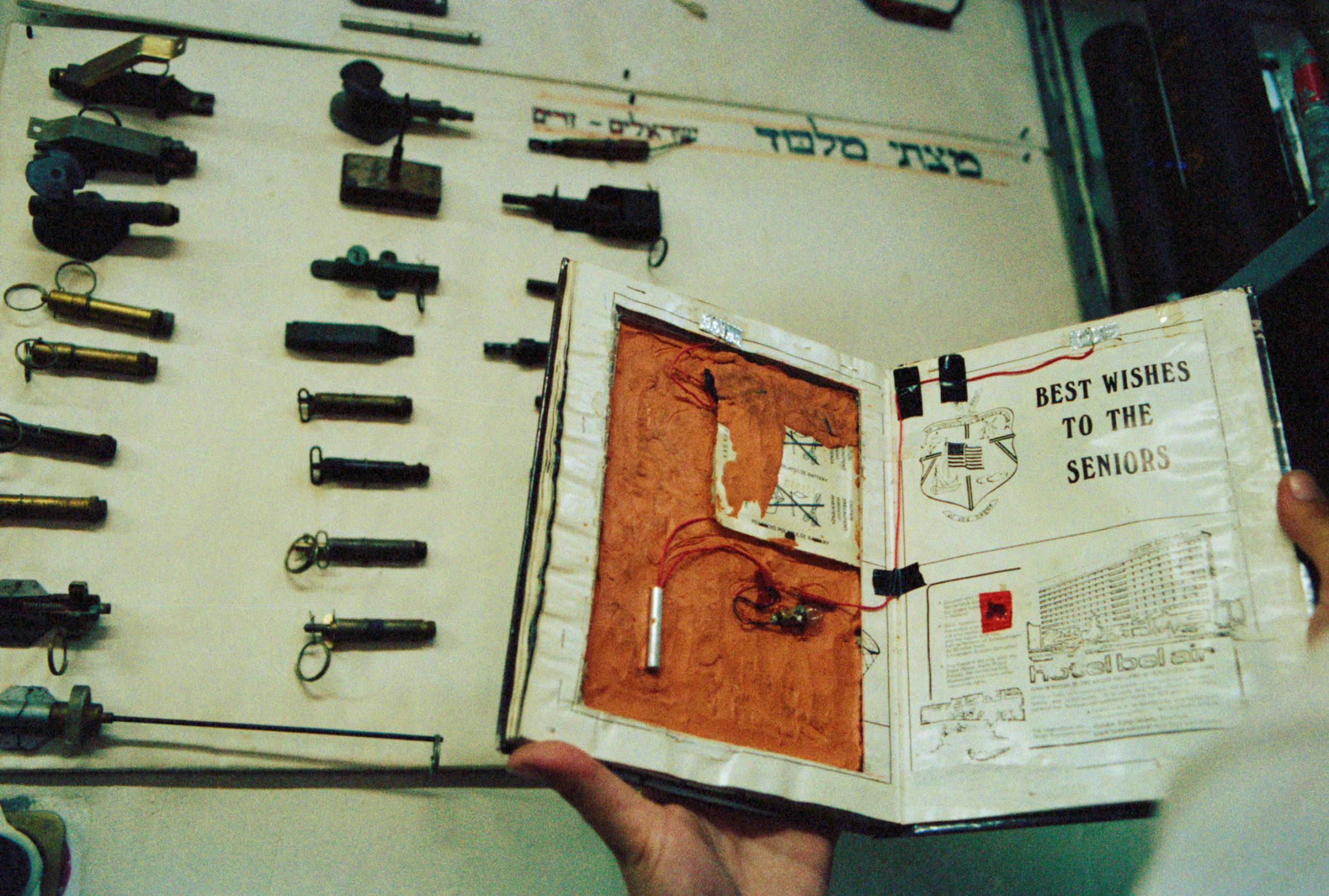 Common objects such as this school yearbook are turned into bombs precisely because they are so tempting for people to pick up. The chart on the wall shows the wide variety of detonators used to set off the explosive charge, which in the case of the book was an easy-to-mold plastic compound.