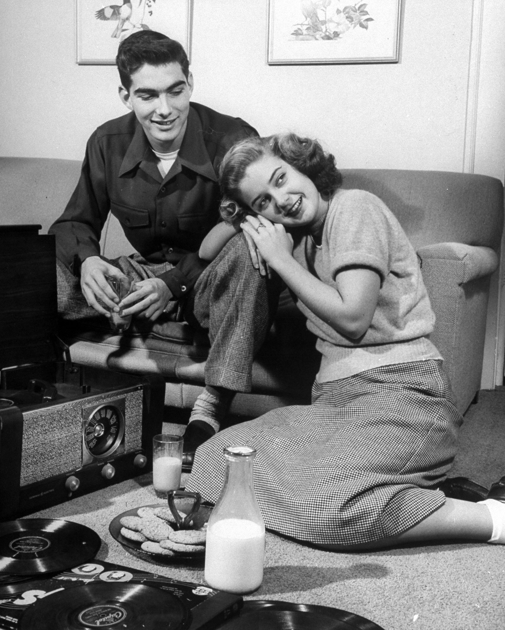 Teenage couple listening to records and having a snack of milk and cookies.