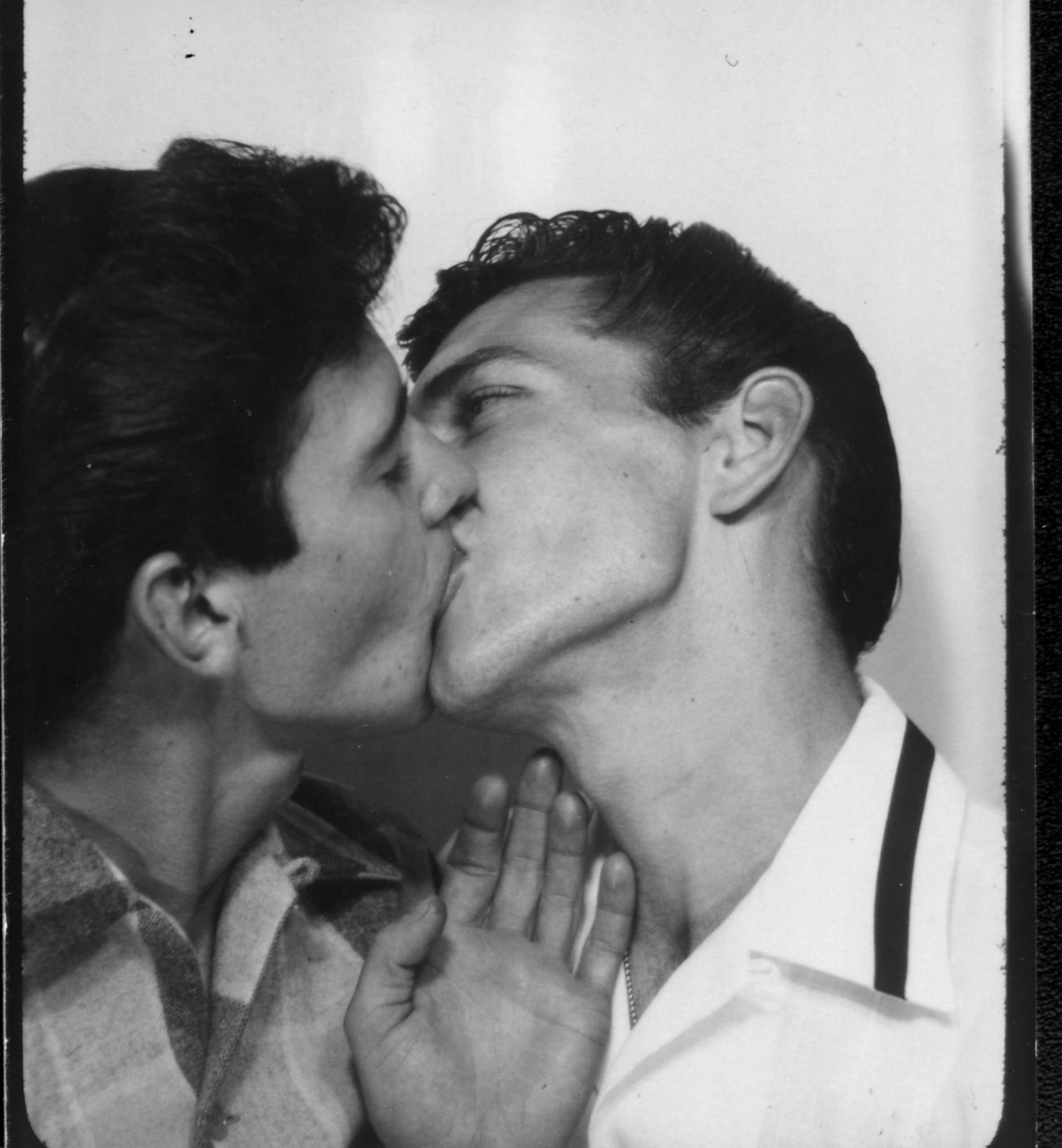 J. J. Belanger kissing a man in a photo booth.  PGE exhibition, Hastings Park.  Vancouver, Circa 1953.
