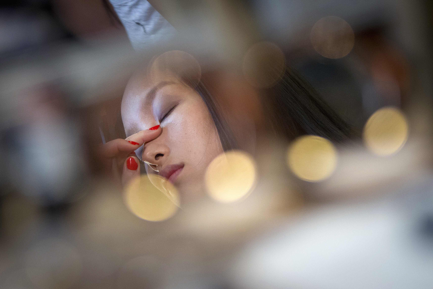 A model is reflected in a mirror as she has her makeup applied before the Donna Karan Spring/Summer 2015 collection show during New York Fashion Week