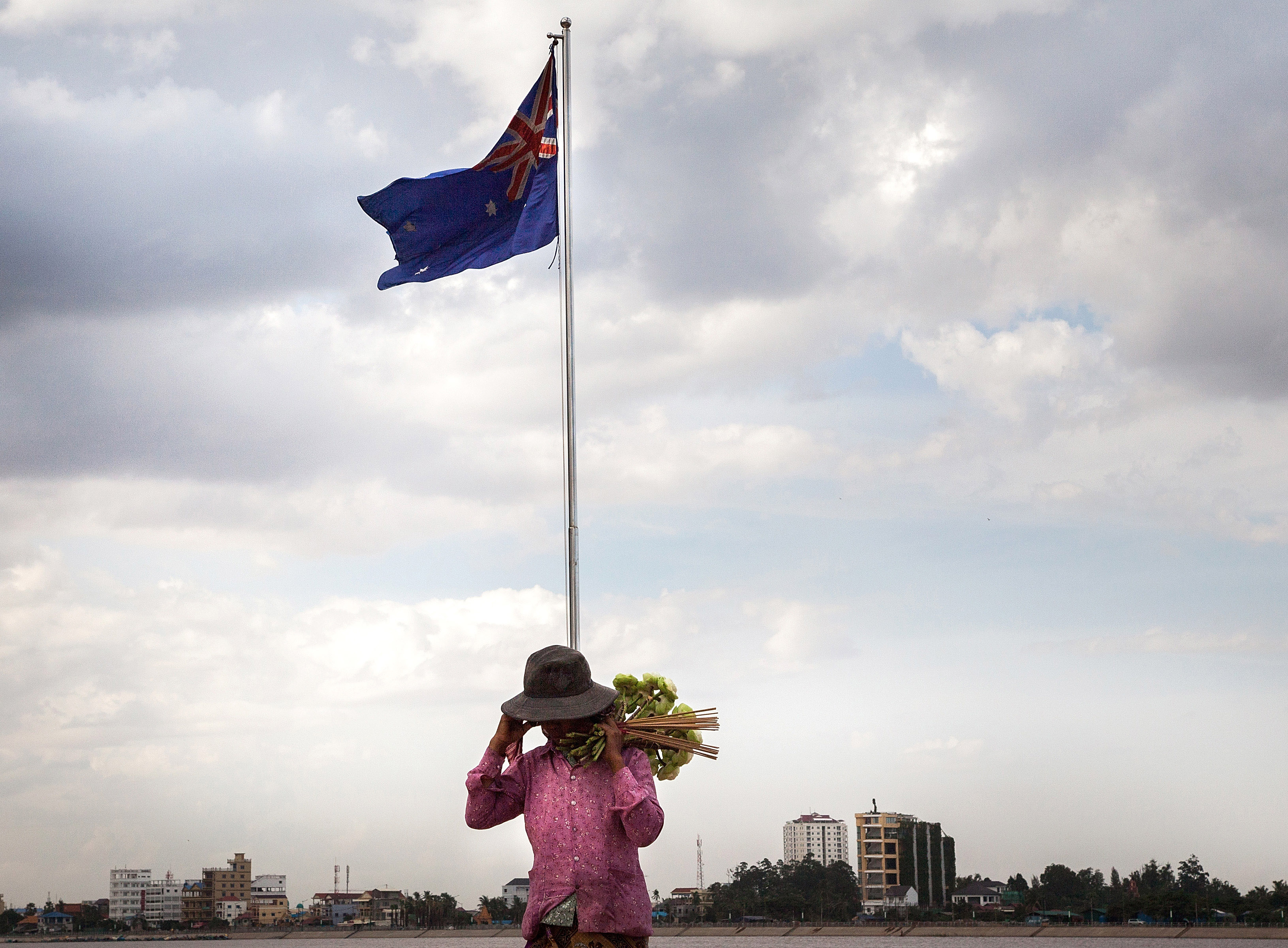 A lotus-flower seller stands underneath the Australian flag along the riverside in Phnom Penh on Aug. 13, 2014. After months of negotiations Australia and Cambodia look set to agree on a deal that will see 1,000 refugees transferred from Australia to Cambodia (Omar Havana—Getty Images)