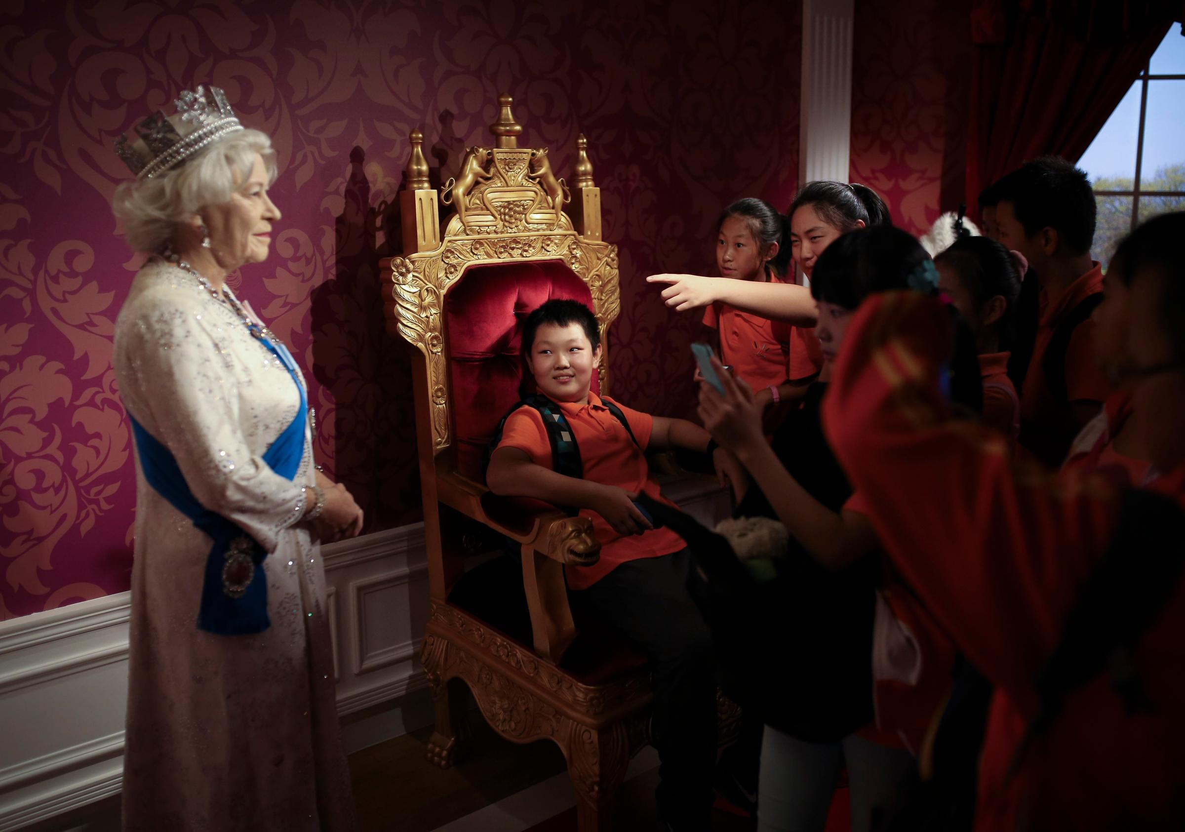 A student sitting on a mock-up of the royalty chair, looks at a wax figure of Britain's Queen Elizabeth II, while others take souvenir photos, at the Madame Tussauds Museum in Beijing on Sept. 19, 2014.