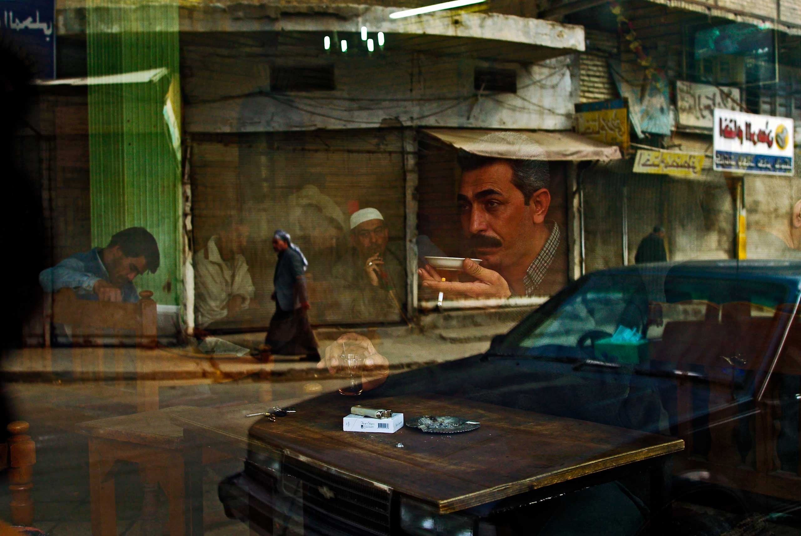 Bruno Stevens, Feb. 12, 2003
                              
                              The window of the Al Zahawi cafe in Rashid Street, named after a famous local poet and musician. Baghdad cafes are a trademark of this ancient city, places where men gather after prayer and play dominoes or blackjack with intense passion while drinking black or lemon tea or traditional arabic coffee (ka-wah). 
                              It was about 6 weeks before the war started that I took this image as a metaphor for the Iraqi population, a complex society whose people are framed by their own divisions and perspectives as well as having their fate determined by the outside world. To this day I believe that I somehow managed to encompass all those tensions and drama still to come in a single frame. I am in Baghdad at the moment, revisiting places and people from 10 years ago, and the Al Zahawi Caf is still one of my favorites.