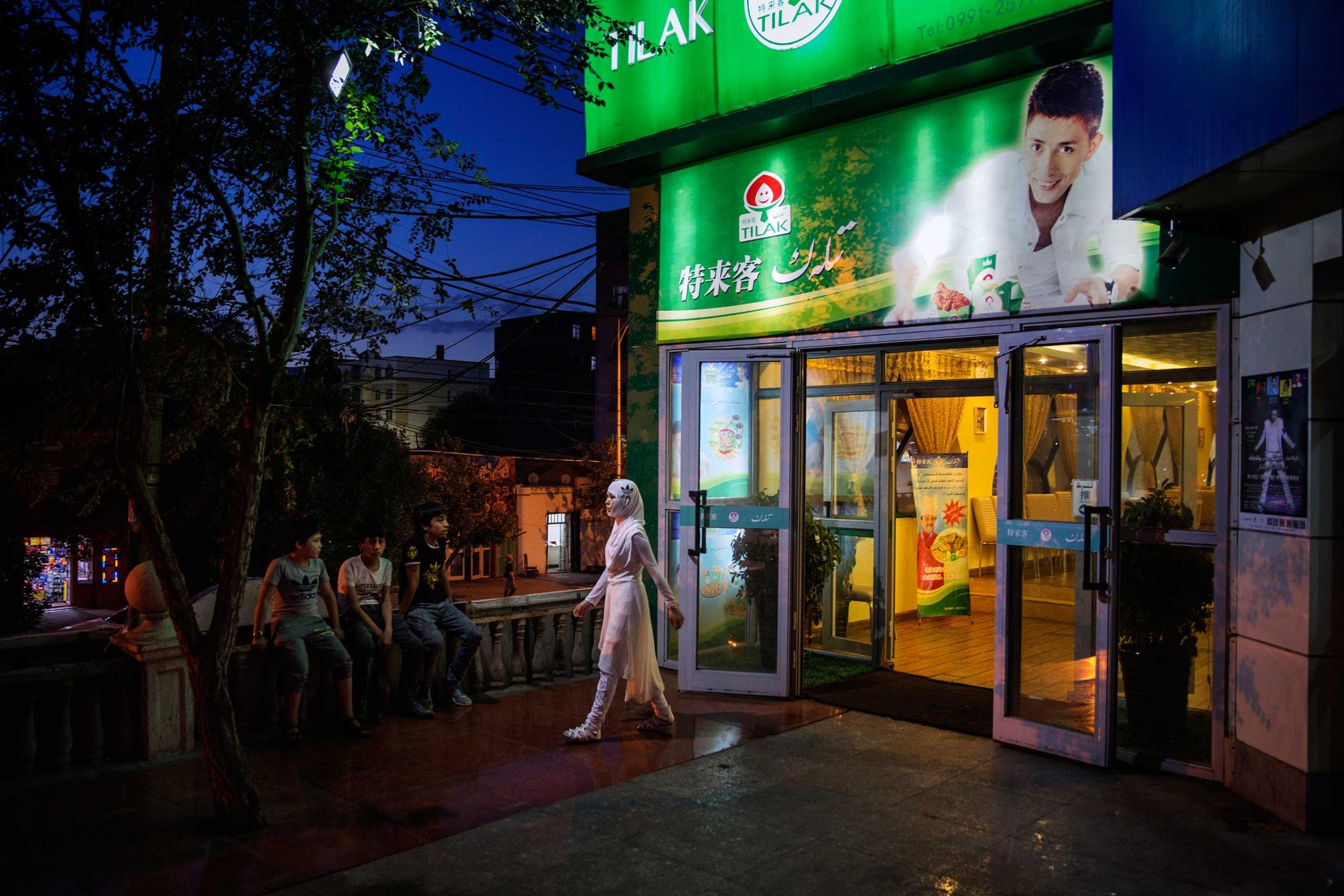 People stand outside a restaurant endorsed by Uighur pop sensation Ablajan, who's picture is on the sign, in Urumqi, China on July 31st, 2014. The performance, held at a state owned broadcasting facility, which Ablajan and his dancers had been preparing for for several weeks, was cancelled an hour before show time. The official reason was due to technical problems but members of the performance admitted it was more likely due to political sensitivities following the recent unrest between Uighurs and Han authorities in Xinjiang.