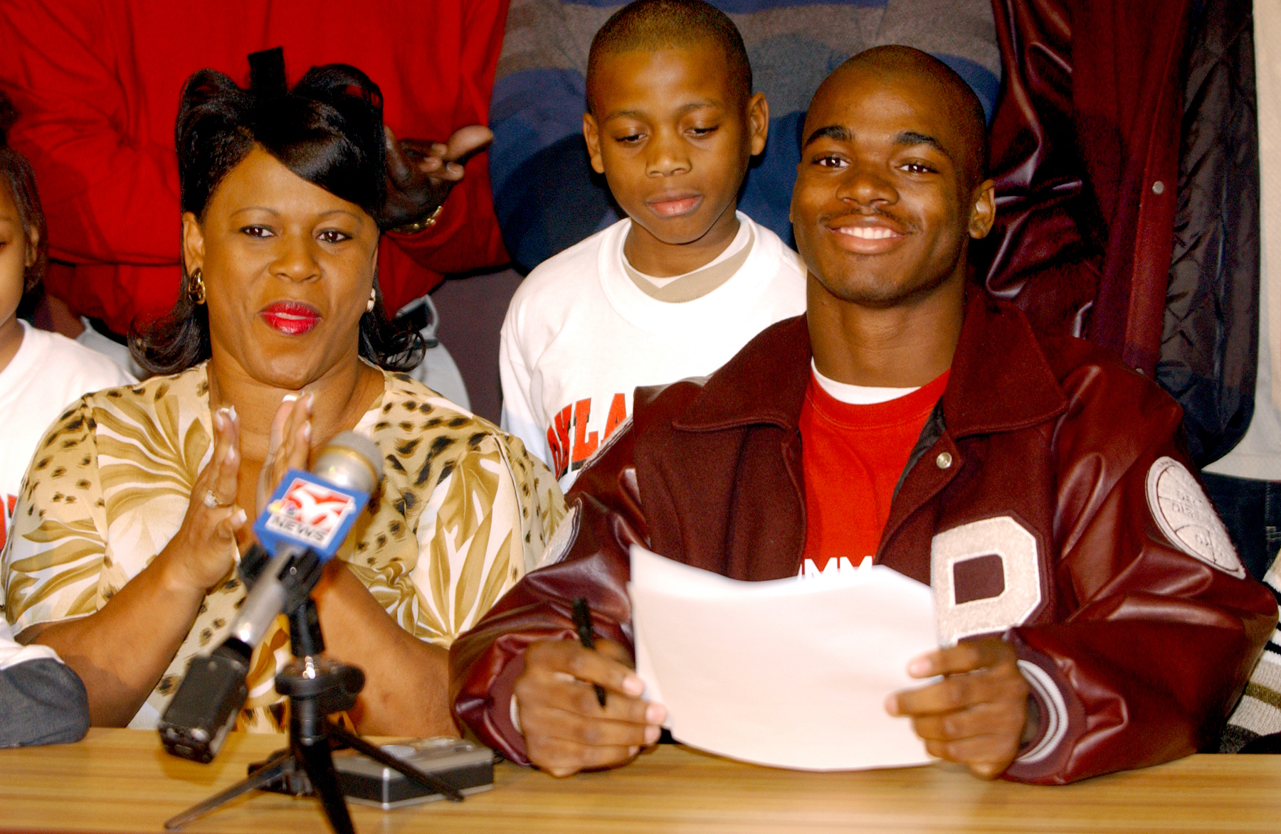 Palestine running back Adrian Peterson, right, smiles after signing a national letter of intent to play football for Oklahoma on Feb. 4, 2004, in Palestine, Texas. At left is his mother Bonita Jackson, and at center is his brother, Jaylon Jackson. (David Branch—Tyler Morning Telegraph/AP)