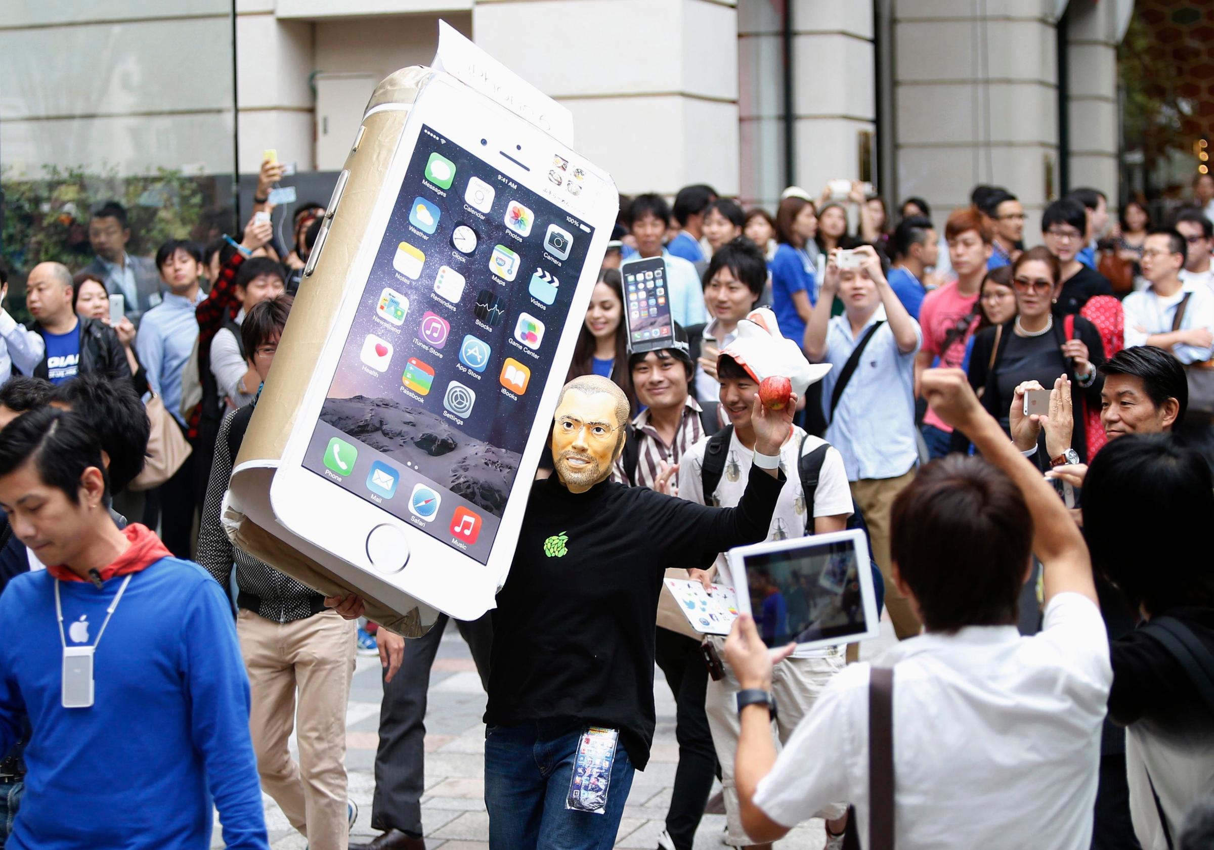 A man wearingaA man wearing a mask depicting Apple's co-founder Steve Jobs holds up a cardboard cut-out of Apple's new iPhone 6, as he walks into the Apple Store in Tokyo on Sept. 18, 2014. a mask depicting Steve Jobs holds up a cardboard cut-out of Apple's new iPhone 6, as he walks into the Apple Store in Tokyo
