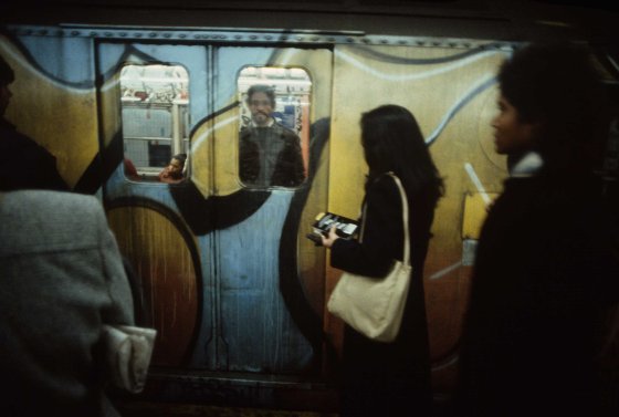 A woman waits to board a train pulling into a station, 1981. Graffiti on the outside of subway cars was usually more elaborate than that inside.