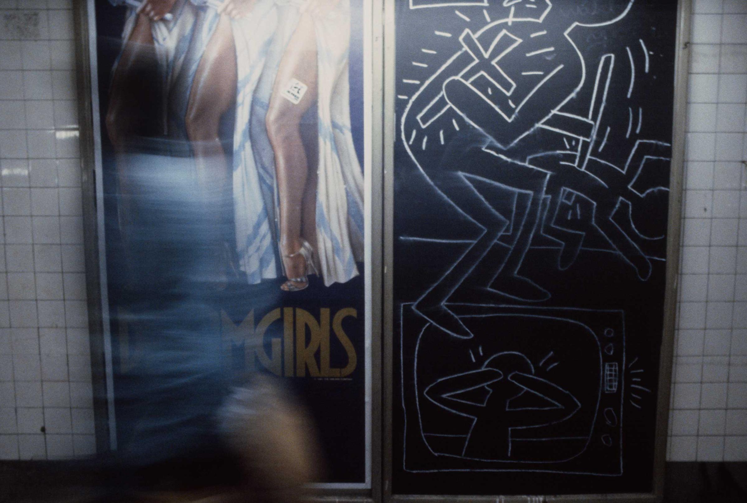 A commuter walks by a poster for the musical Dreamgirls and a Keith Haring chalk drawing, 1981.