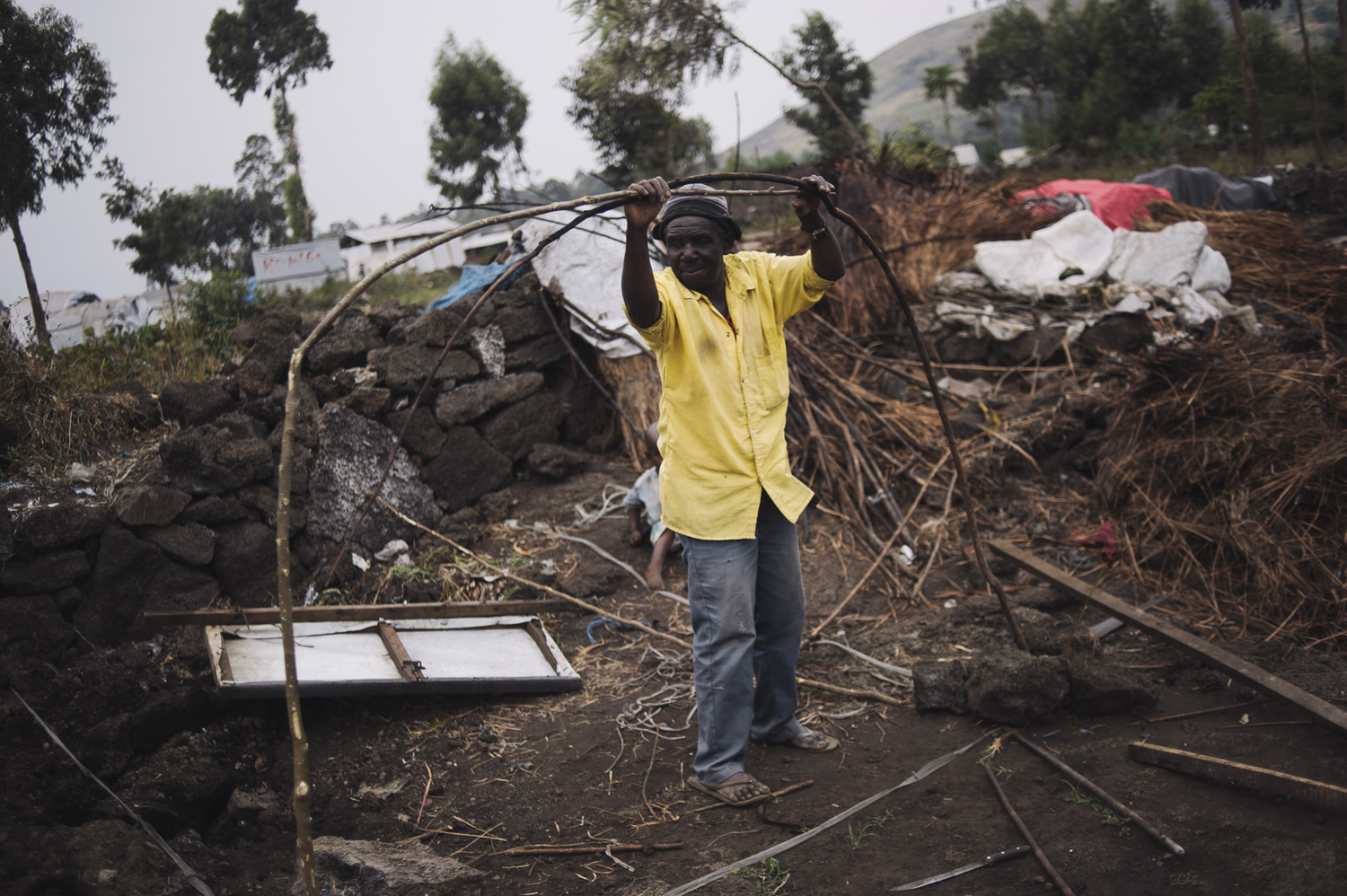 A displaced Congolese man rebuilds his makeshift shelter from sticks and volcanic rock in the Bulengo site for the internally displaced. Many of the original huts here were covered with grasses for the roofing, and many now have tarpaulin sheeting, which still provides only scant cover against the cold and the rain in the harsh environment of the camp, July 15, 2014.