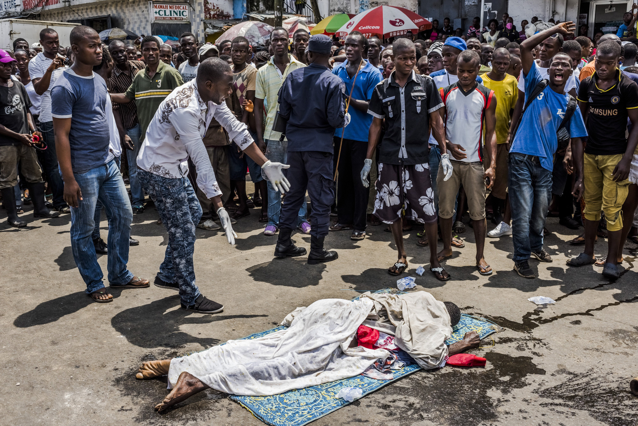 Residents look on as the body of a man suspected of dying from Ebola lies in a busy street, after it was reportedly dragged there to draw attention of burial teams following days of failed attempts by his family to have his body picked up, in Monrovia, Liberia, Sept. 15, 2014. (Daniel Berehulak—The New York Times/Redux)