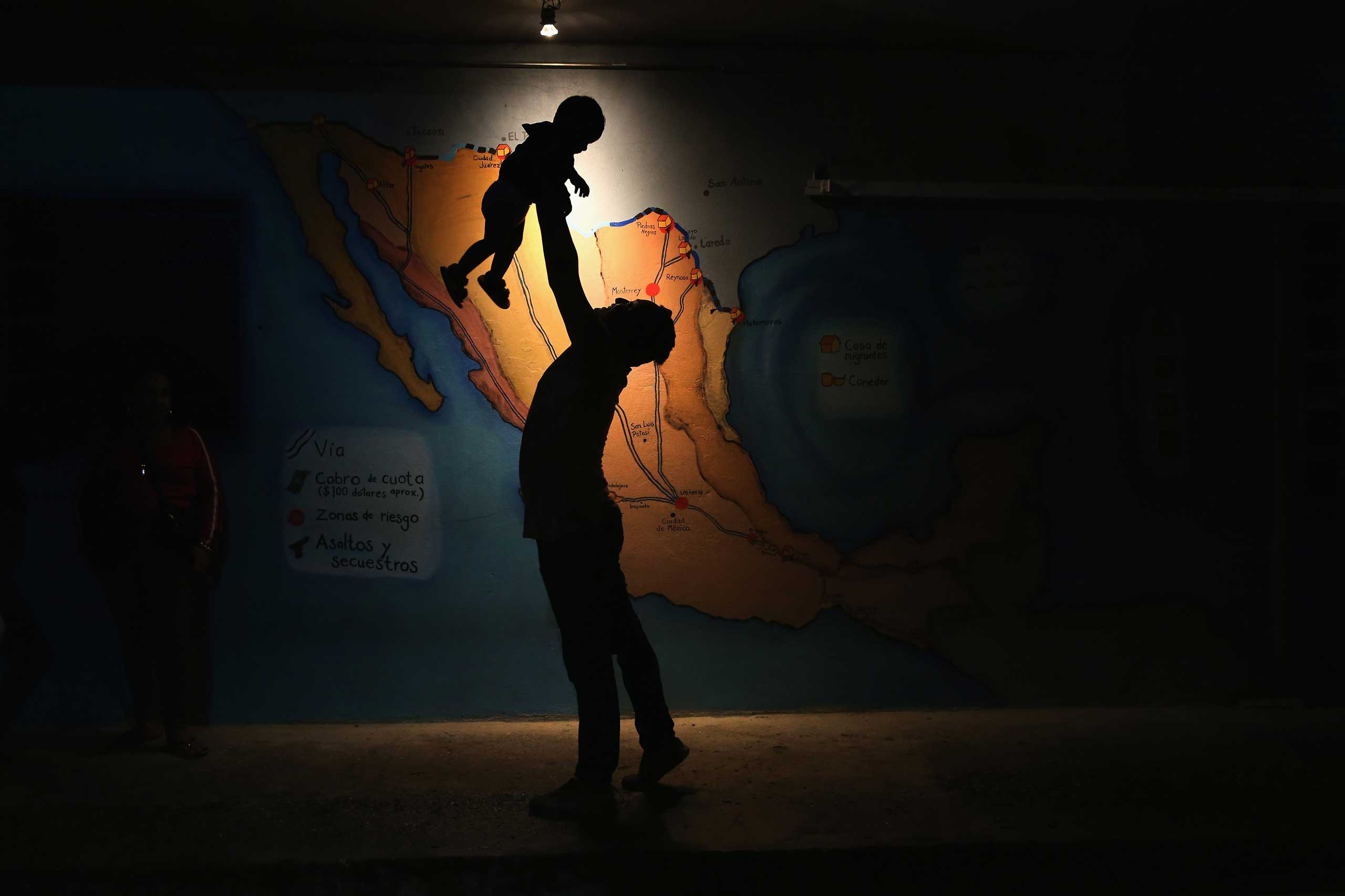 A Honduran immigrant entertains a fellow immigrant's child in front of a map of Mexico on September 14, 2014 in Tenosique, Mexico.