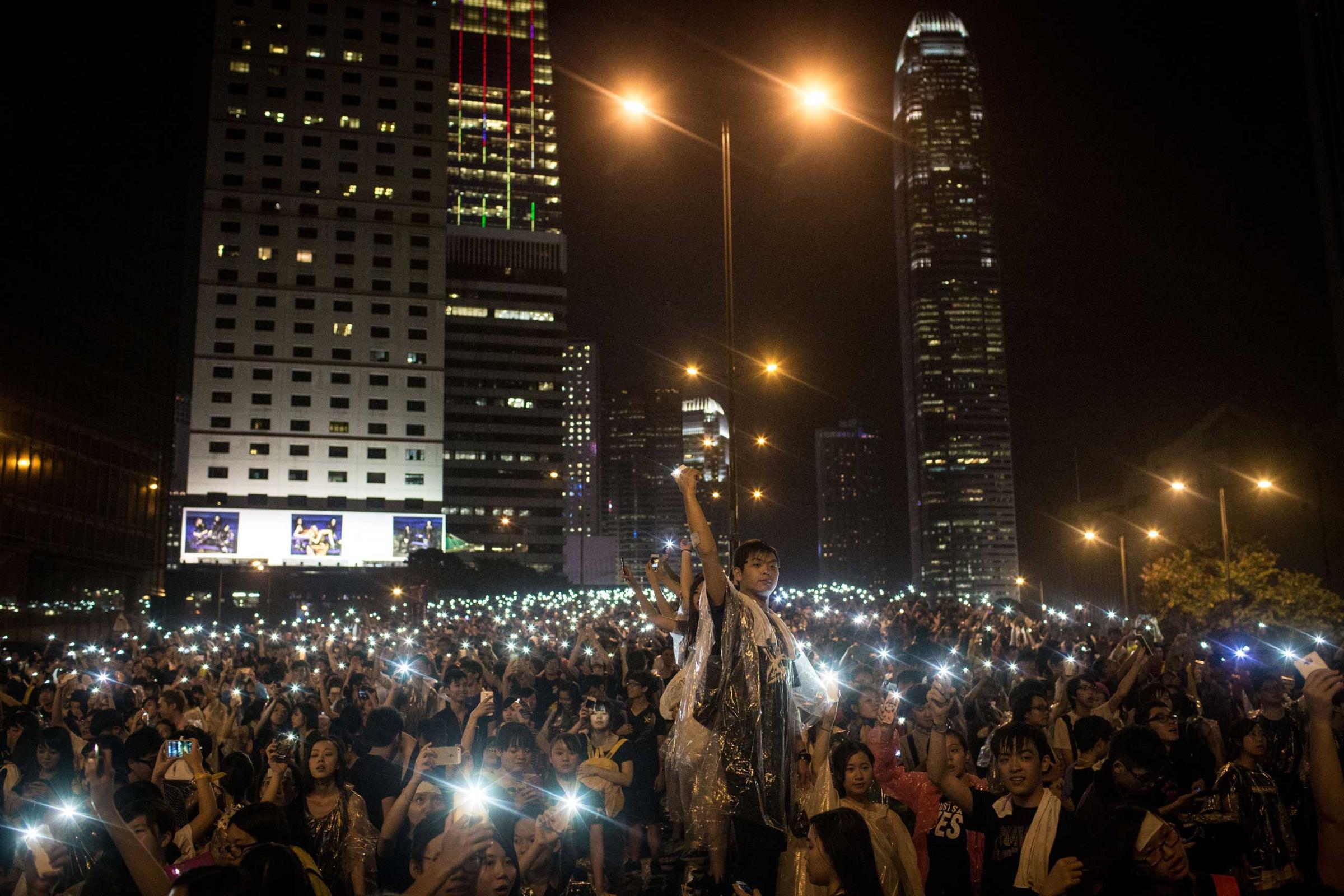 Protesters sing songs and wave their cell phones in the air after a massive thunderstorm passed over outside the Hong Kong Government Complex on Sept. 30, 2014 in Hong Kong, Hong Kong.