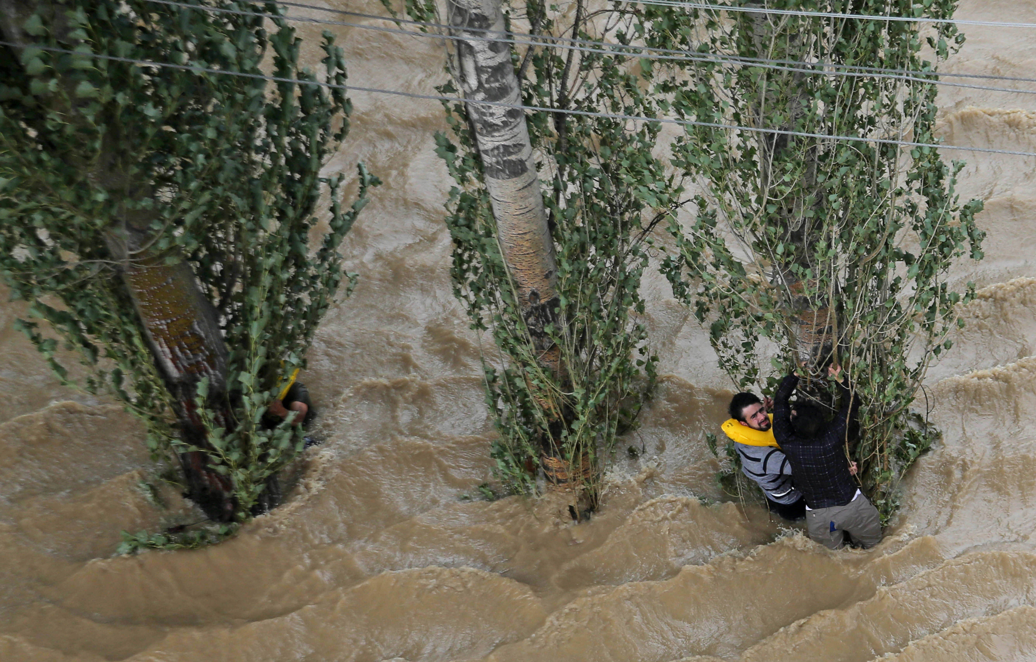 Kashmiris hang on to a tree to prevent being swept away by floodwaters in Srinagar, India, Sept. 9, 2014.